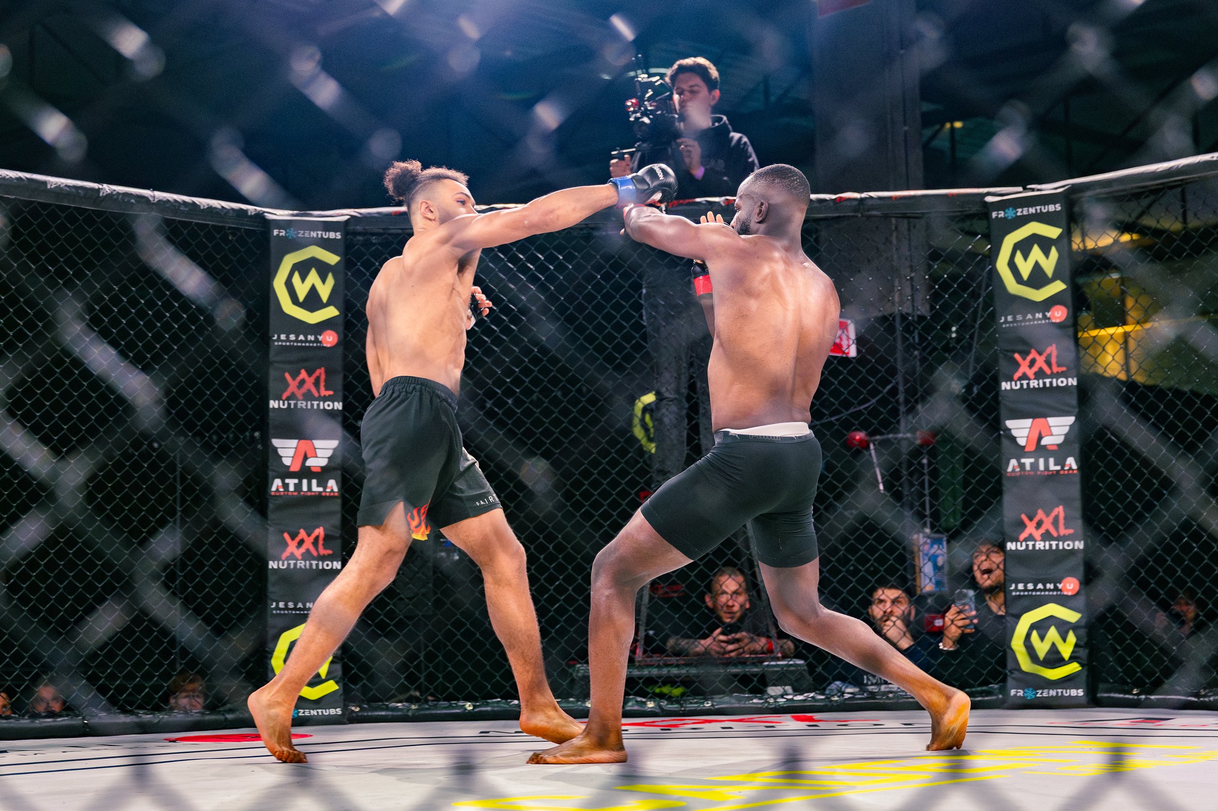 Twee jonge mannen vechten in een mixed martial arts wedstrijd in een octagon, met een cameraman die het gevecht filmde op de achtergrond.