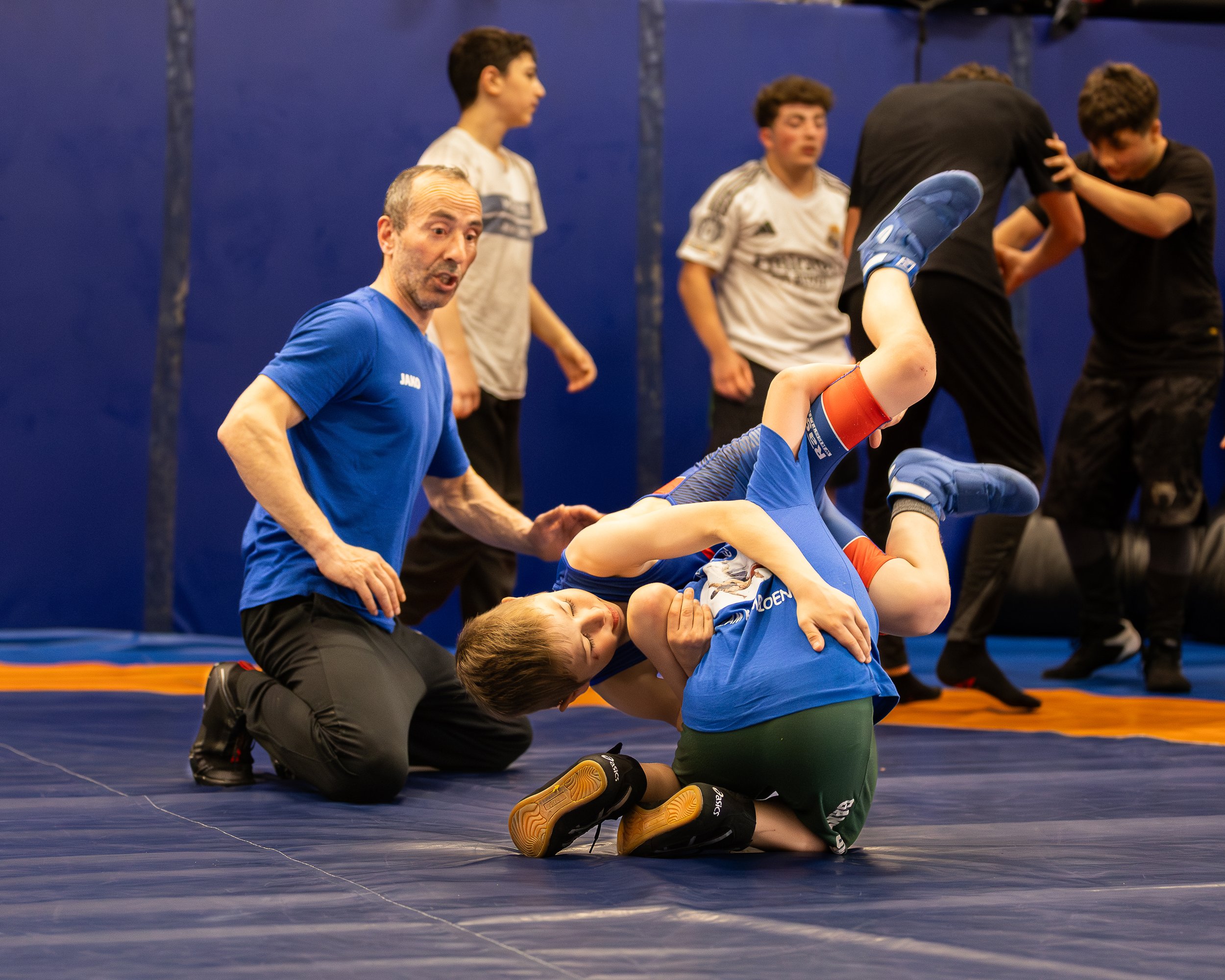 Een sportcoach helpt jonge atleten tijdens een oefening op een sportmat in een gymzaal.