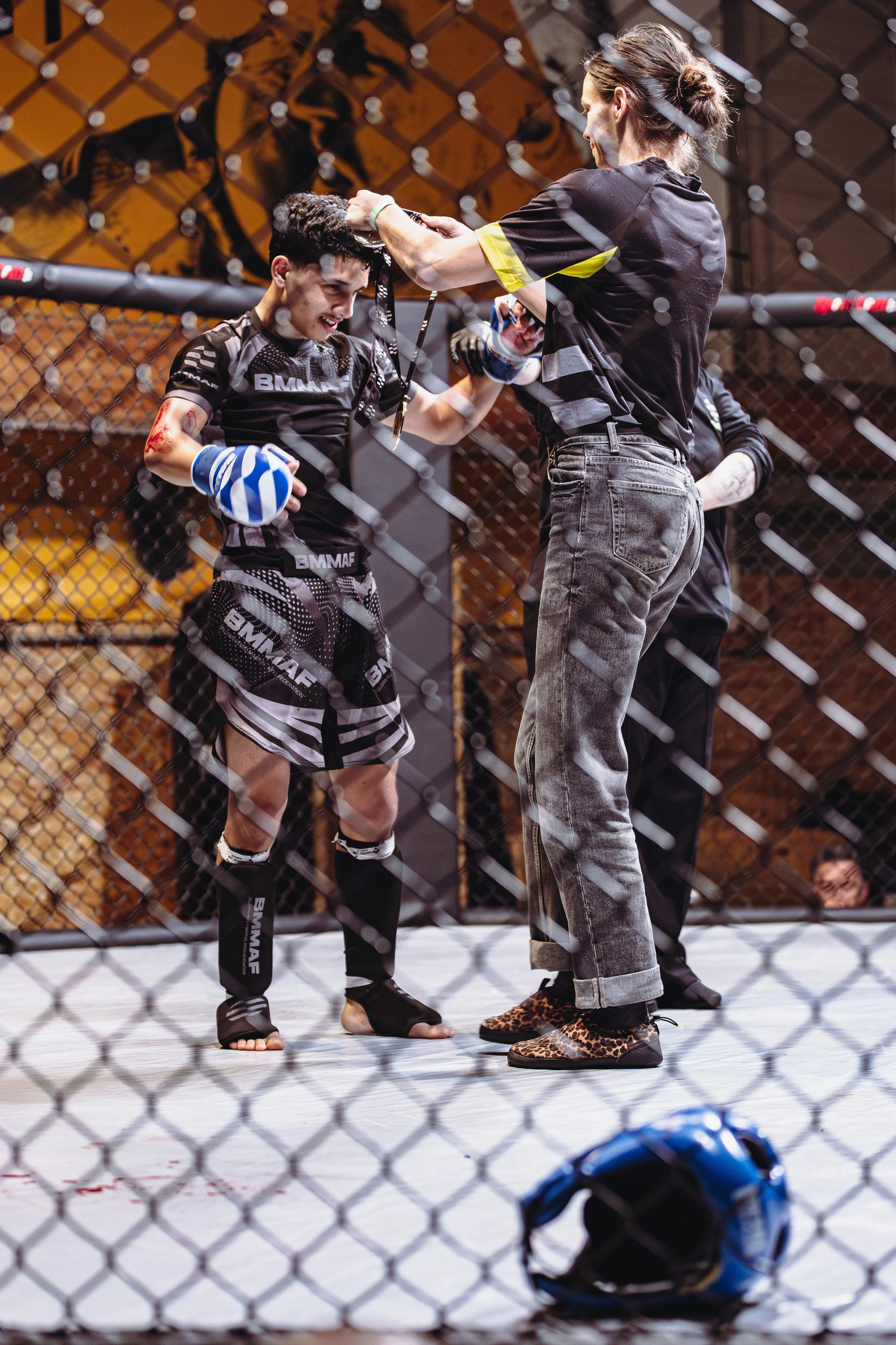 Een vrouwelijke MMA-vechter ontvangt een medaille na haar gevecht in de octagon, met haar coach die haar feliciteert en haar hand vasthoudt.