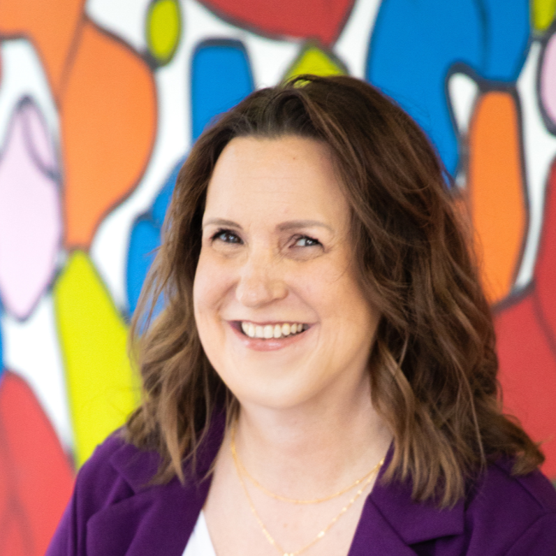 Kim Ast photo sitting in front of a colorful wall