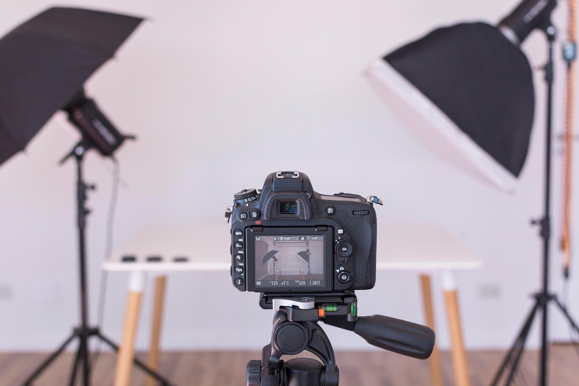 A professional camera on a tripod captures a white background with studio lighting equipment in a photography studio setup.