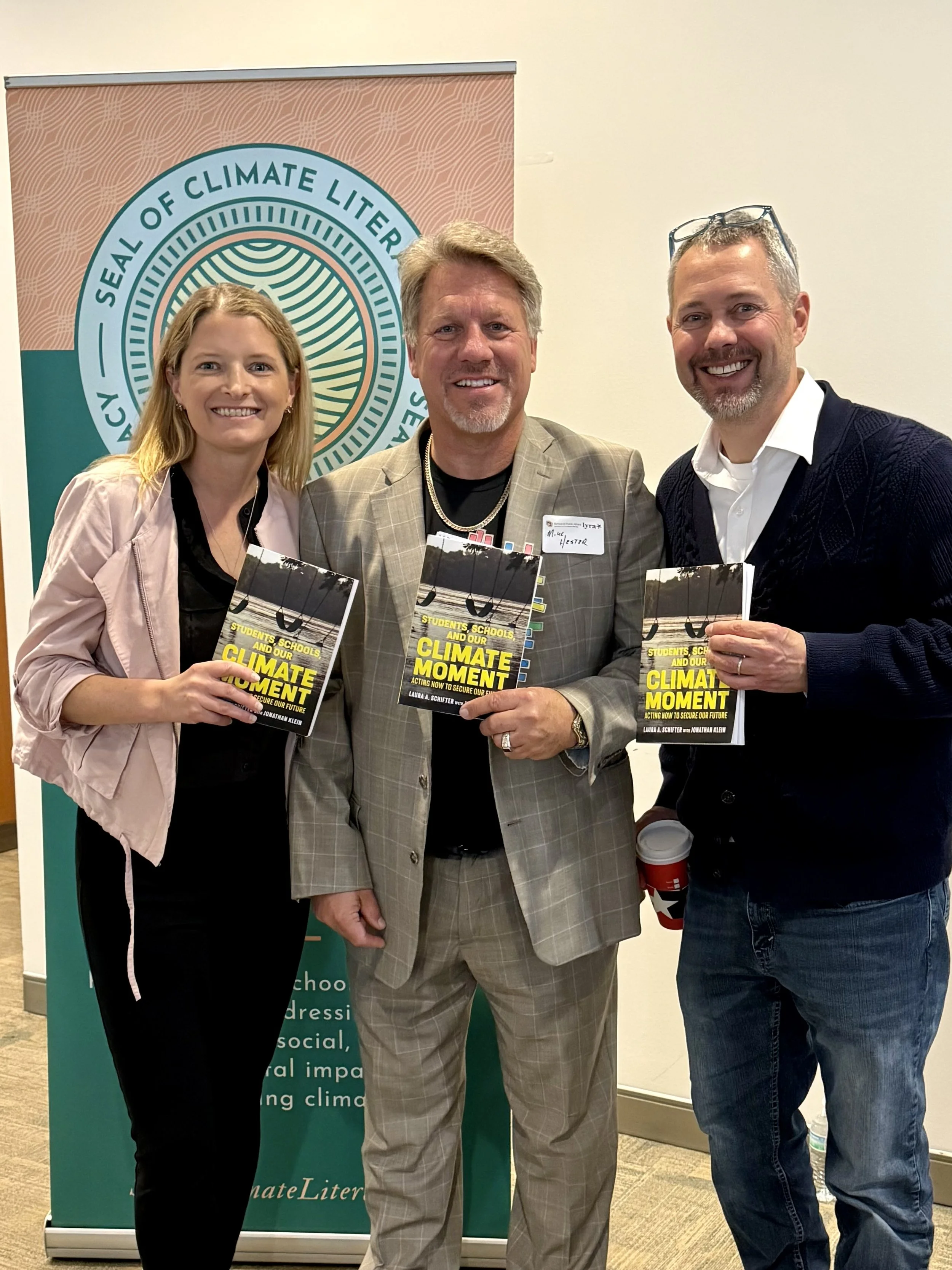 Three people together holding book with climate literacy seal sign in background