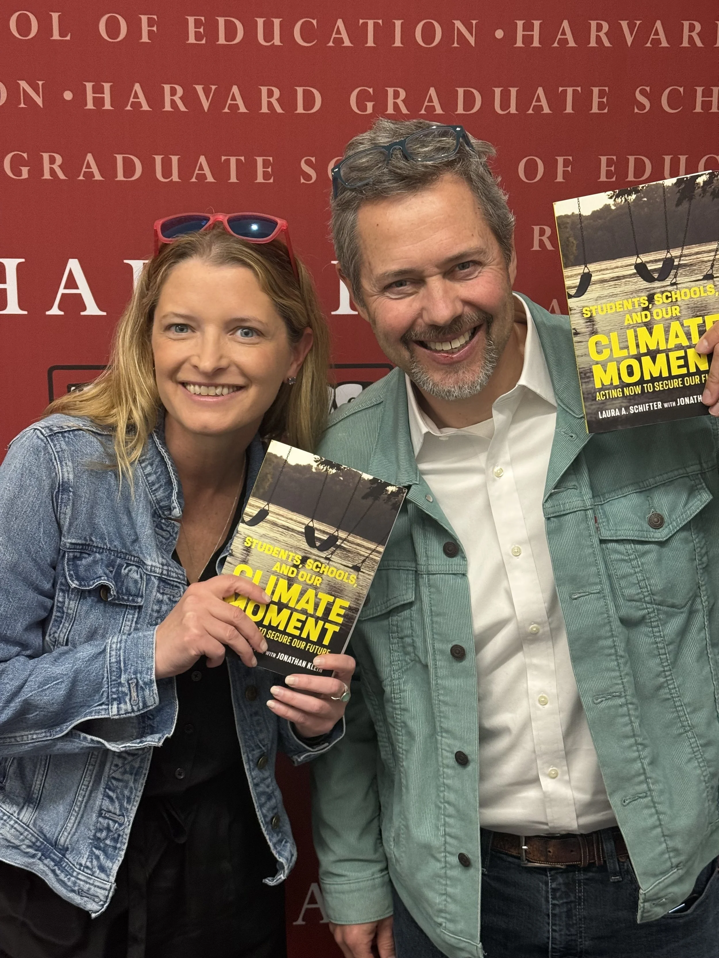 Laura and Jonathan holding book with Harvard sign in background