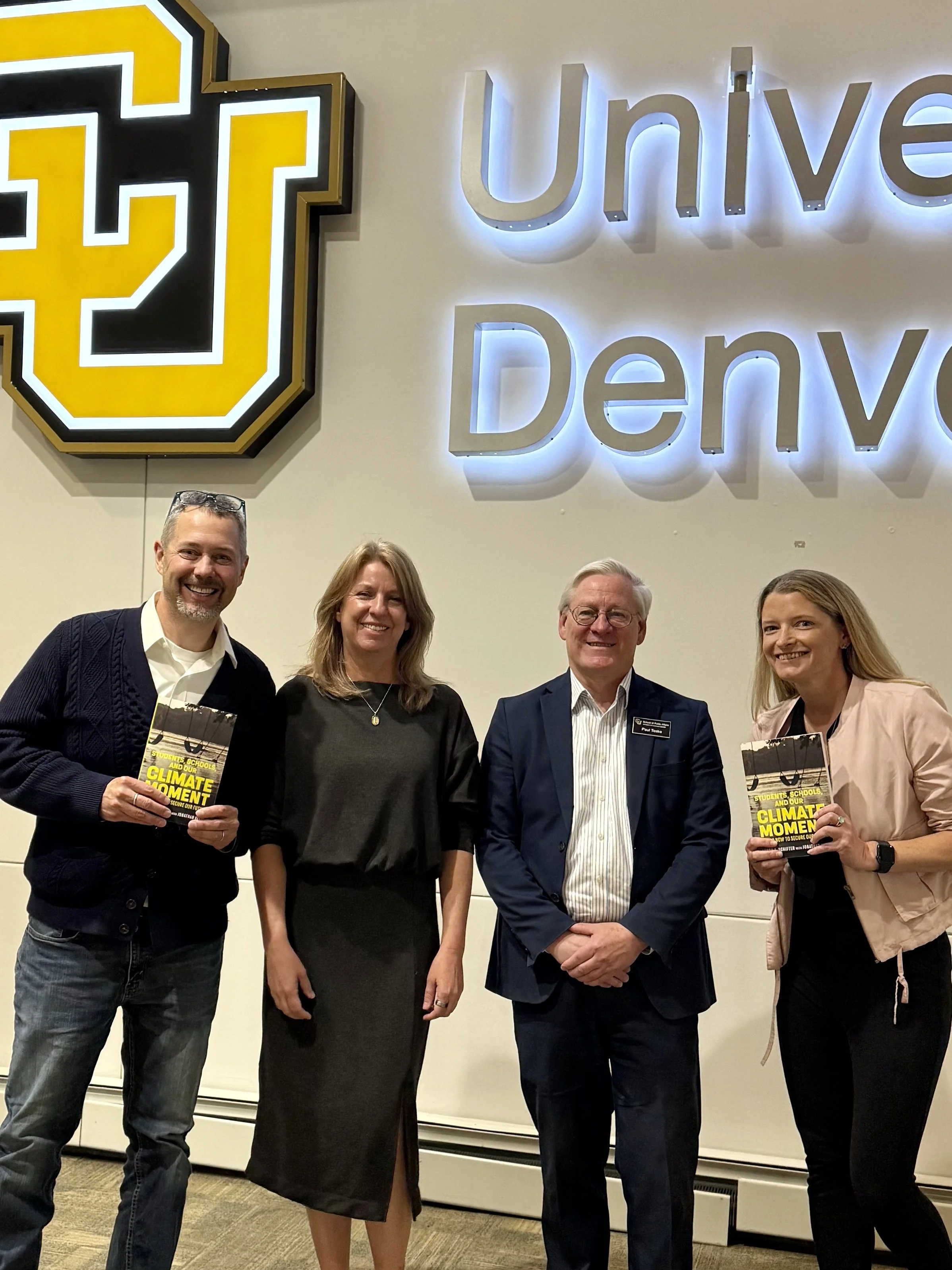 four people two holding book with CU Denver sign on wall