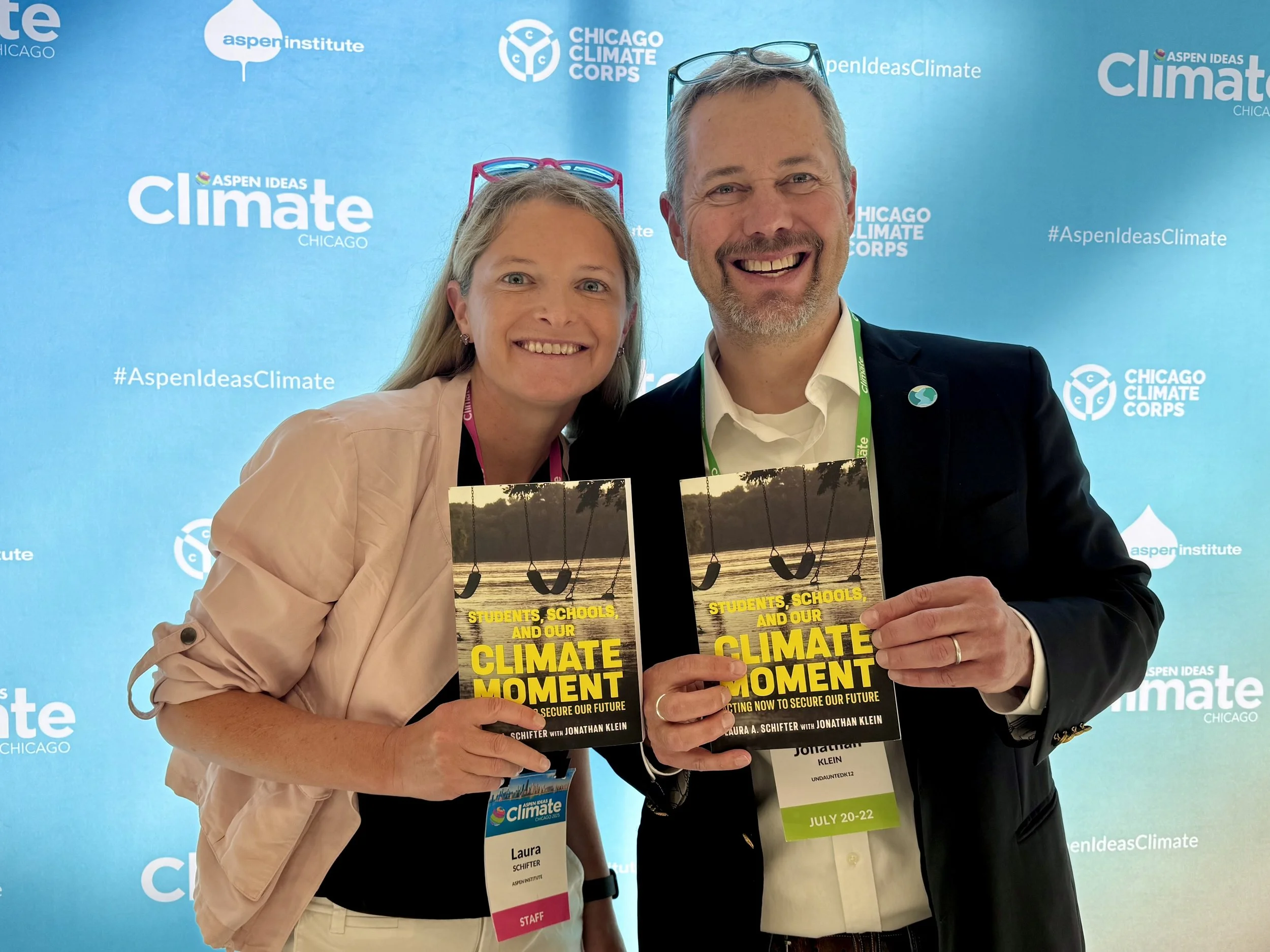 Laura and Jonathan holding book with Aspen Ideas climate background
