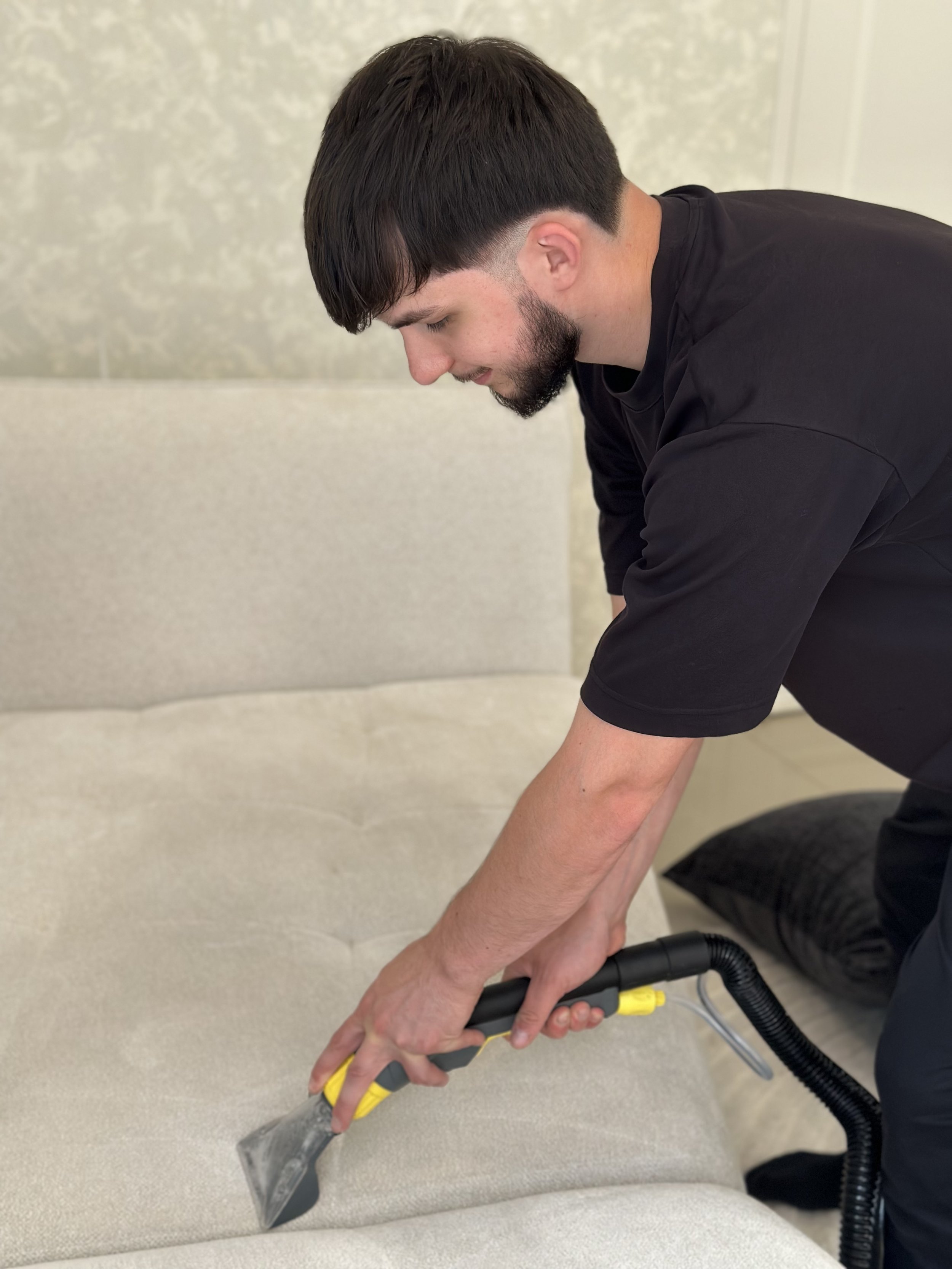 Homme nettoyant un canapé beige avec un aspirateur à main.
