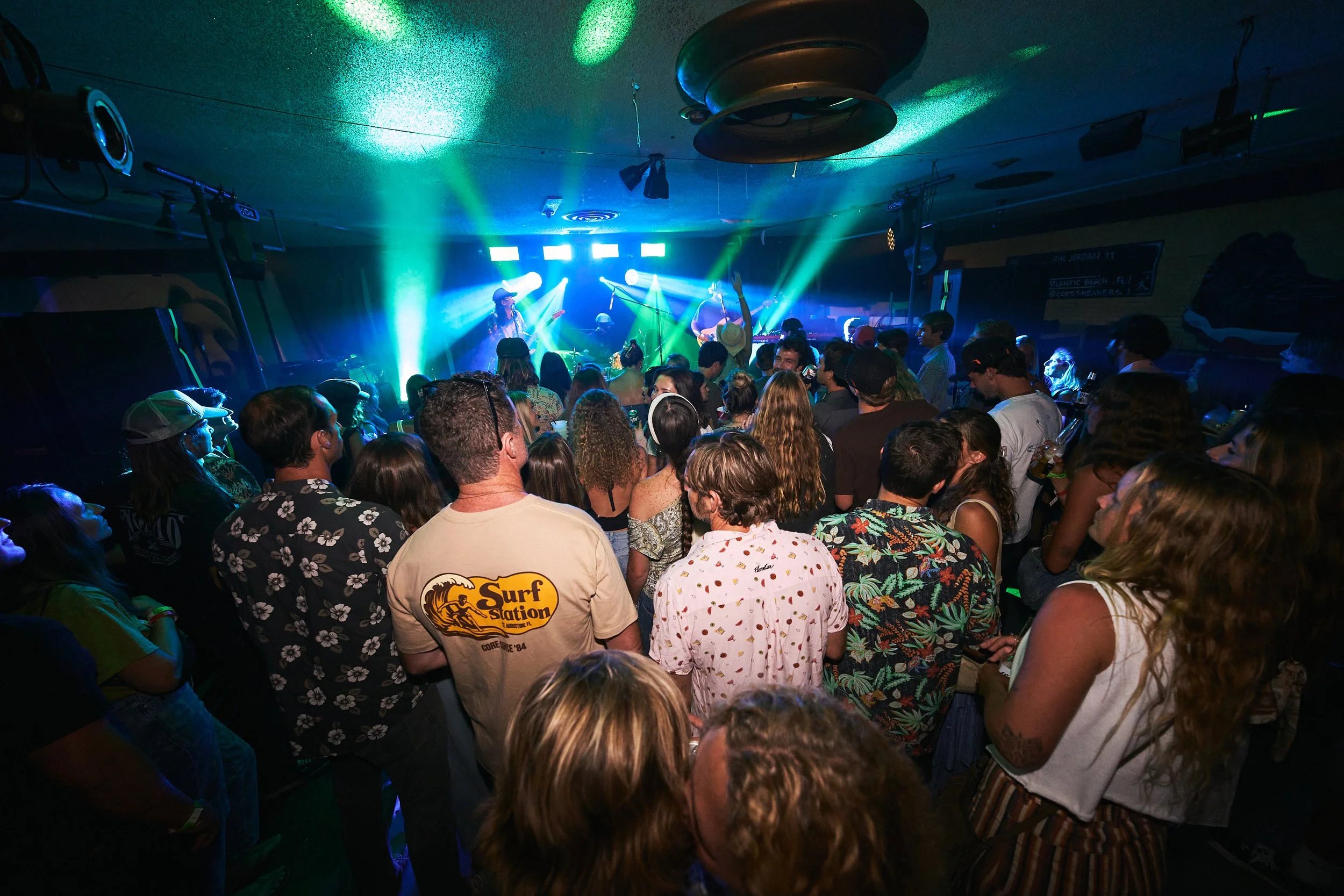 Crowd of people at a live music concert with a band performing on stage and colorful lights.