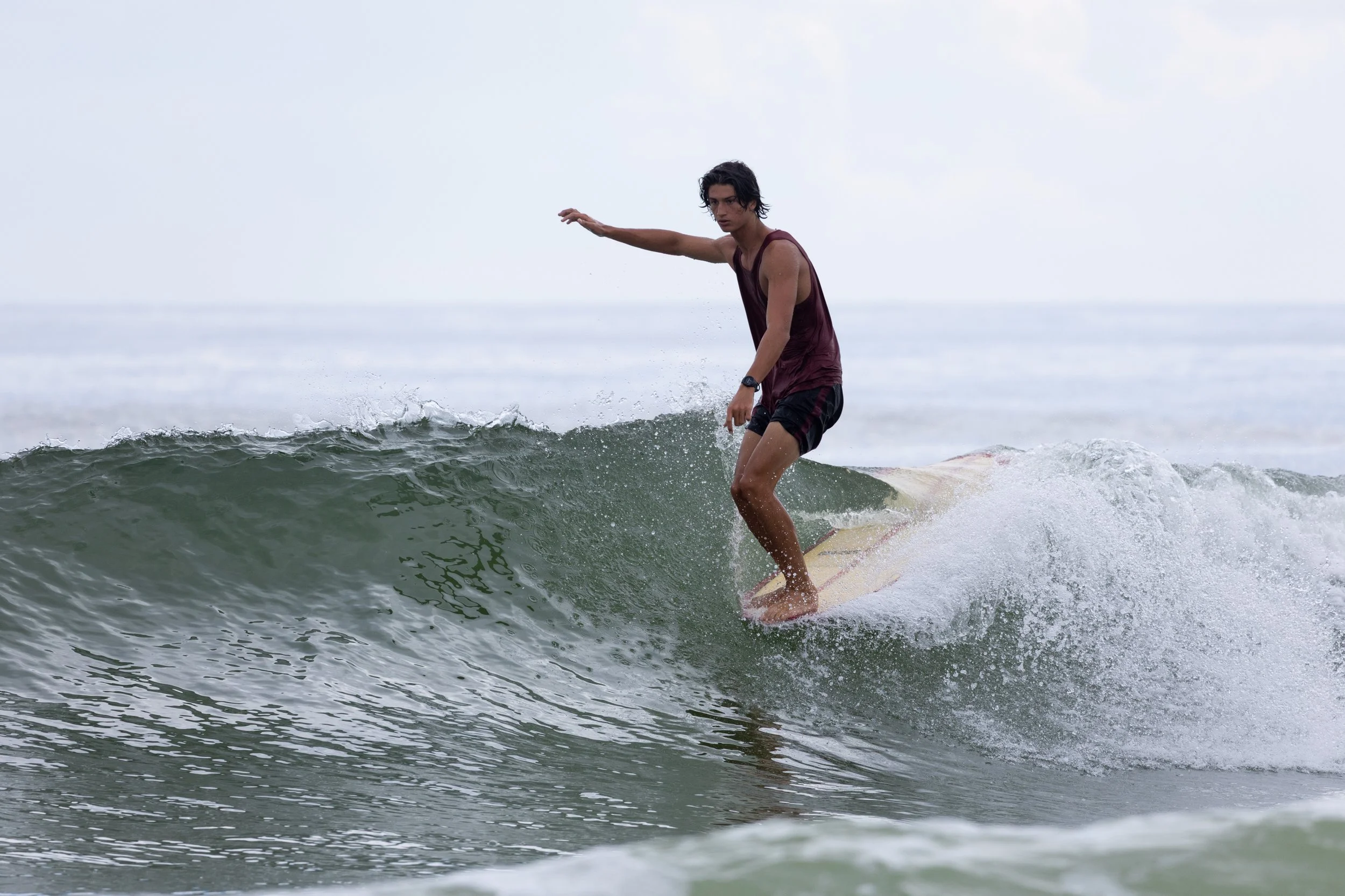 A young man surfing on a wave in the ocean on a cloudy day.