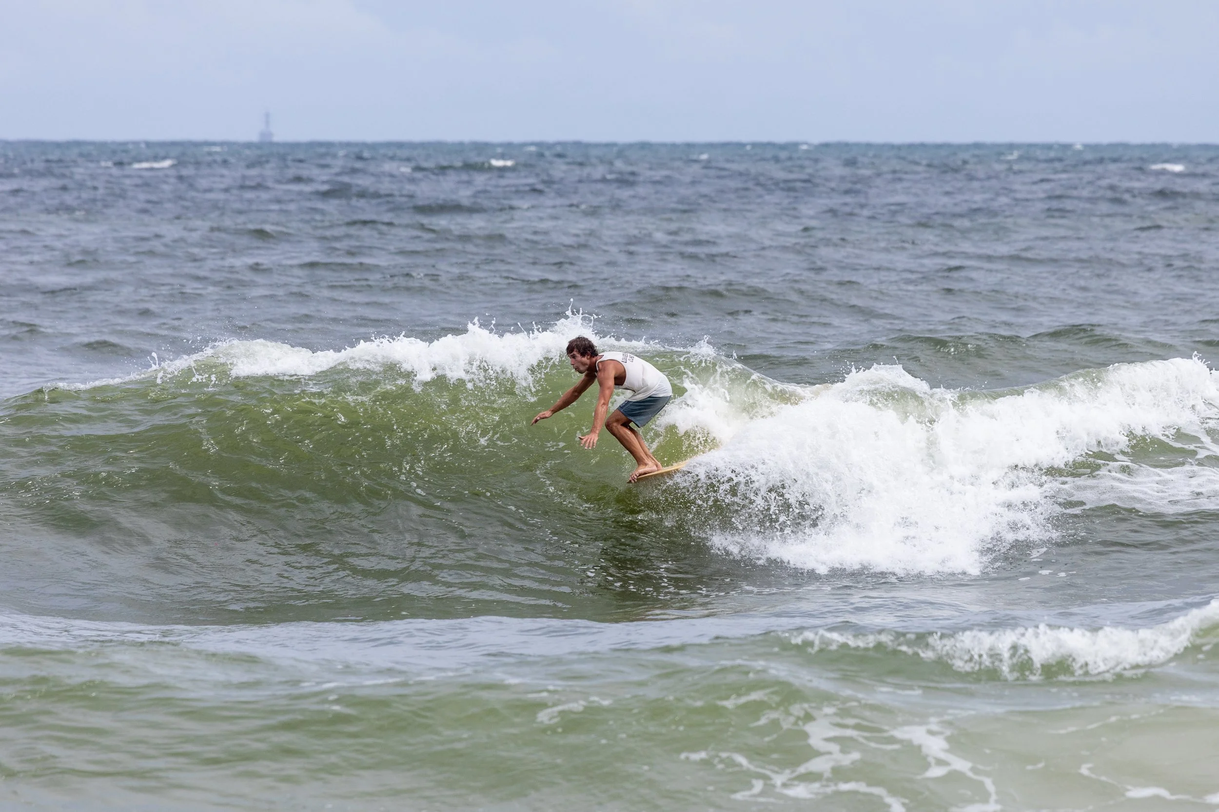 A person surfing on a small wave in the ocean, with a distant boat on the horizon.