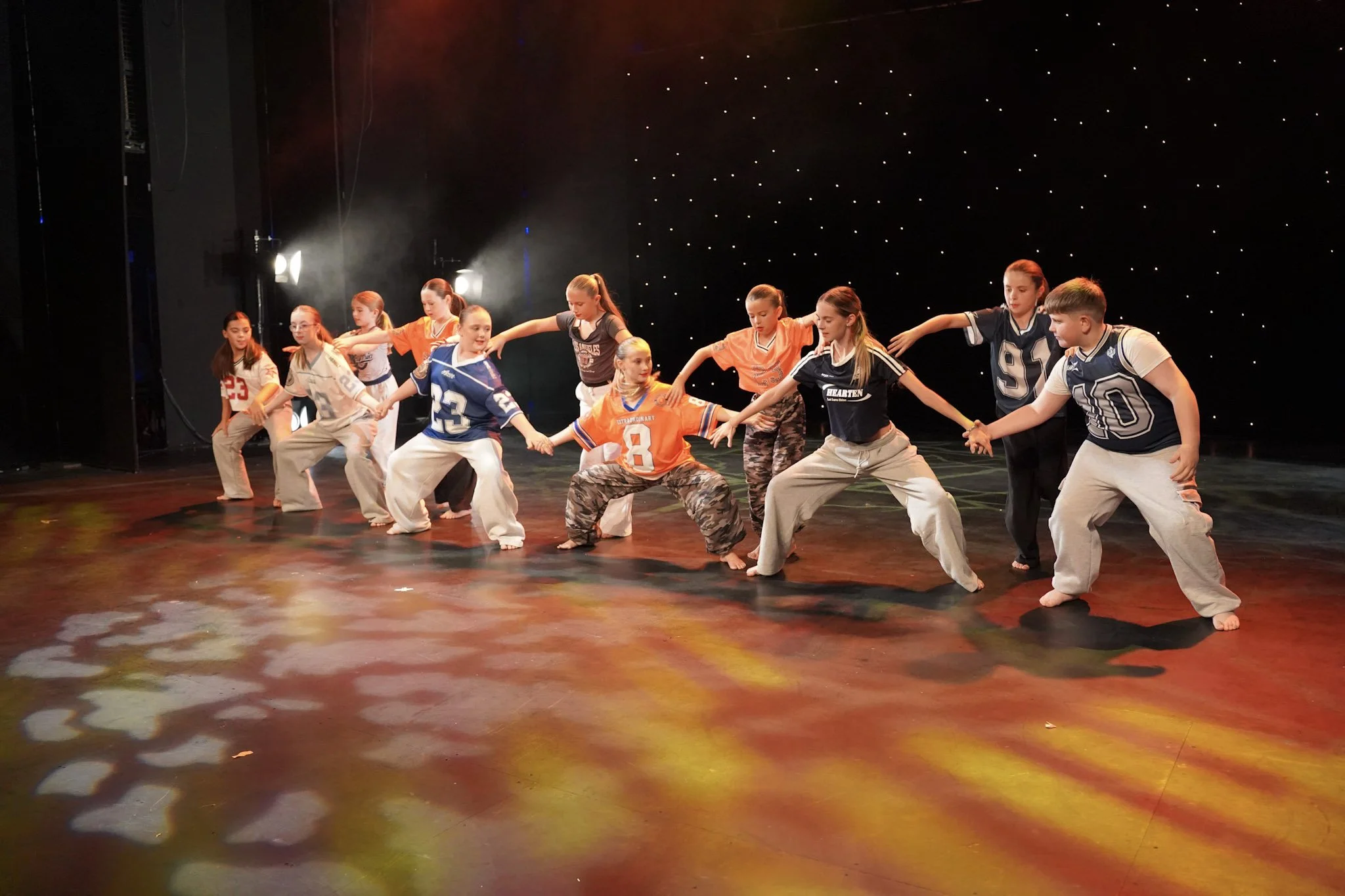 A group of children performing a dance on stage, holding hands and crouching down.
