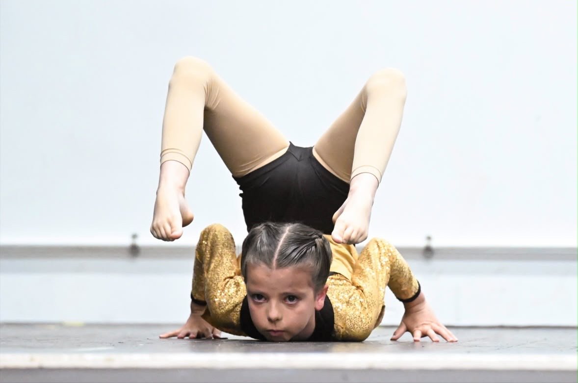 Young girl performing a contortion pose on the floor, with her head and hands on the ground and legs bent over her shoulders.