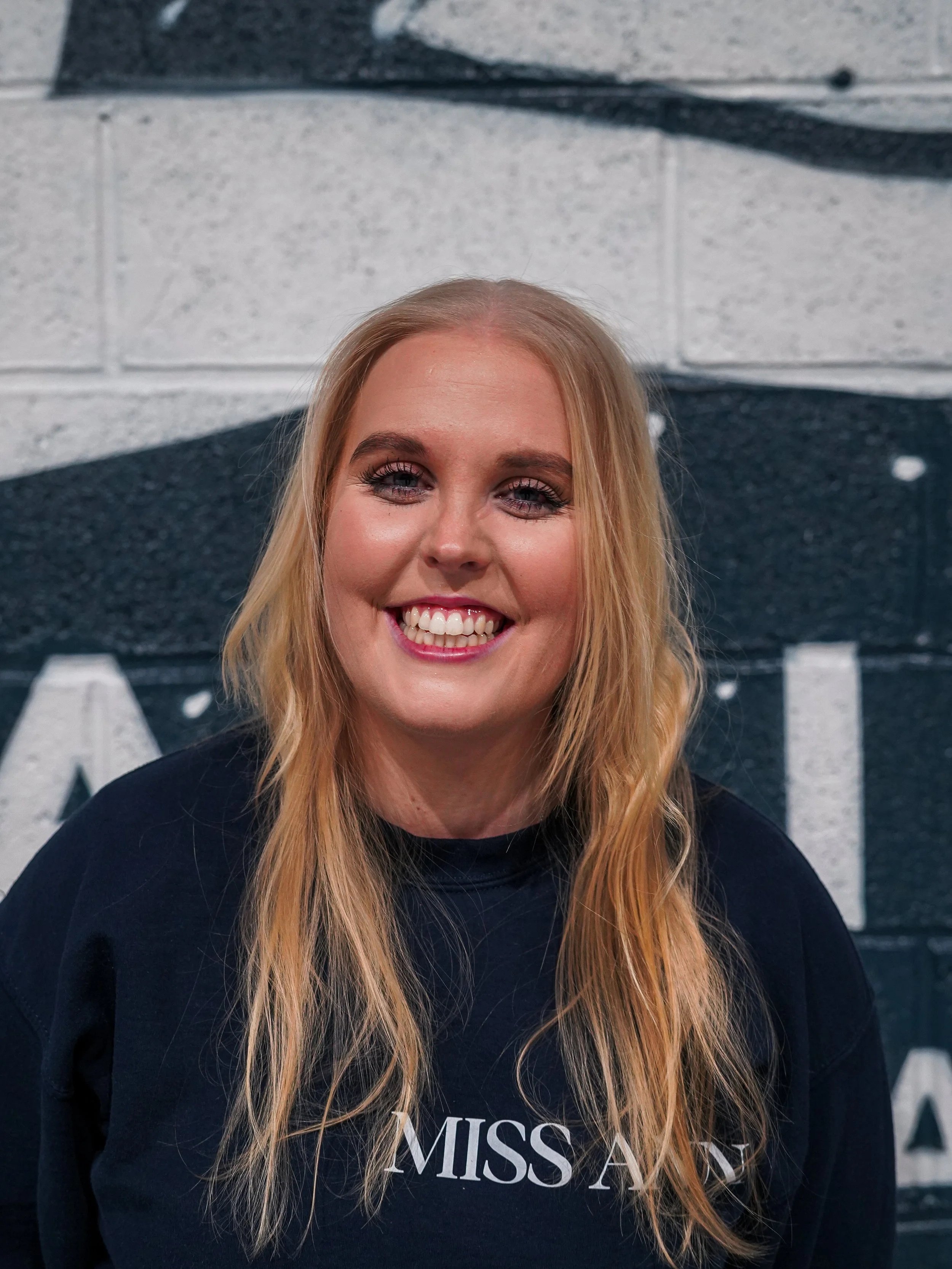 A woman holding a young child against a black brick wall with a large white letter 'D' painted on it.