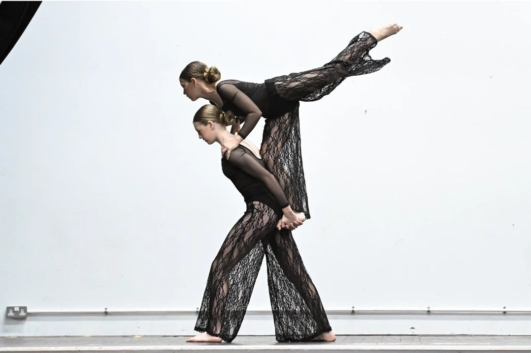 Two women dressed in black lace outfits performing a balancing act, with one woman standing on the other's back and holding one leg extended behind her.