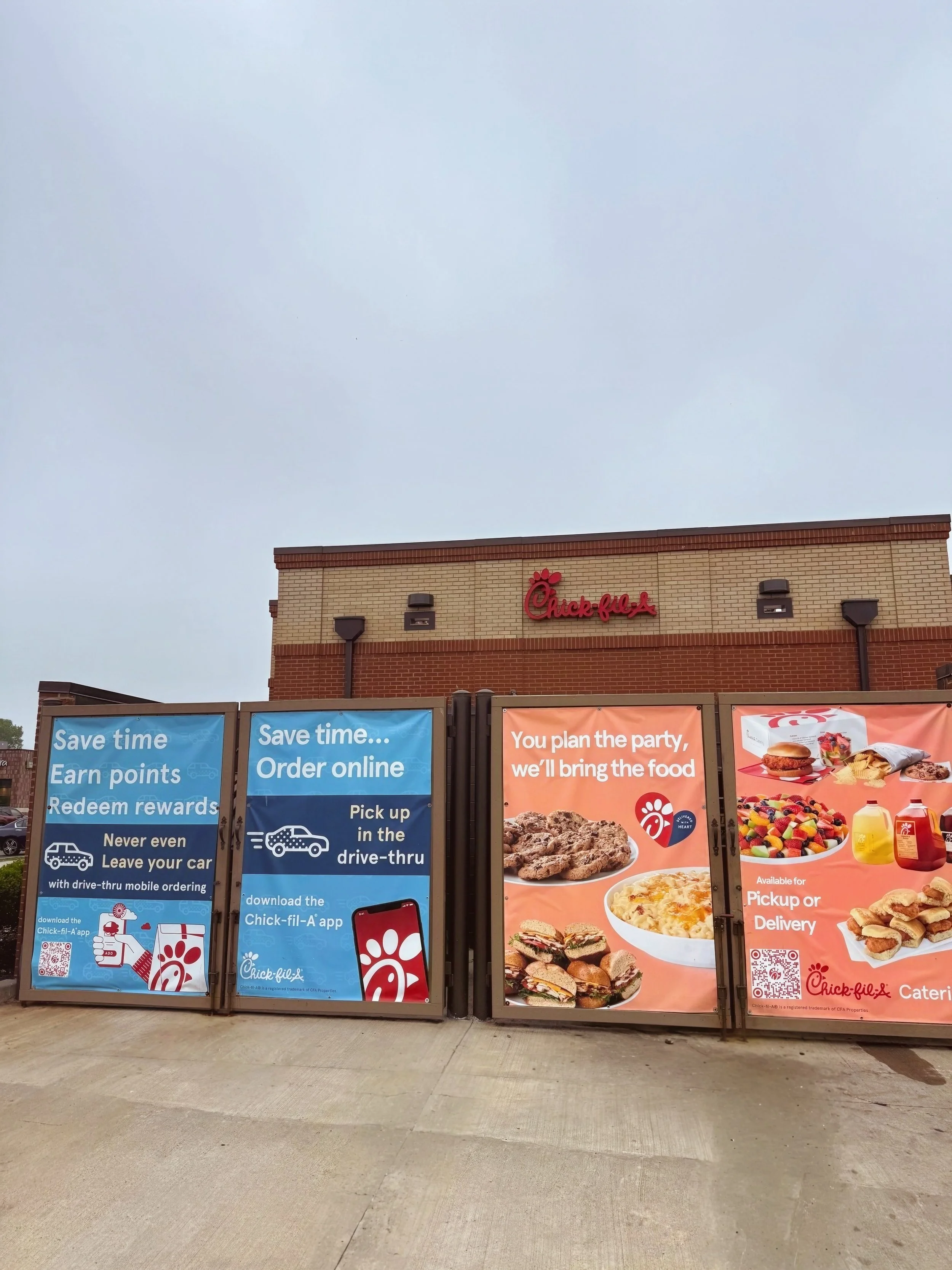 Chick-fil-A restaurant exterior with promotional signs about online ordering and food delivery, displaying pictures of chicken, sandwiches, and sides.