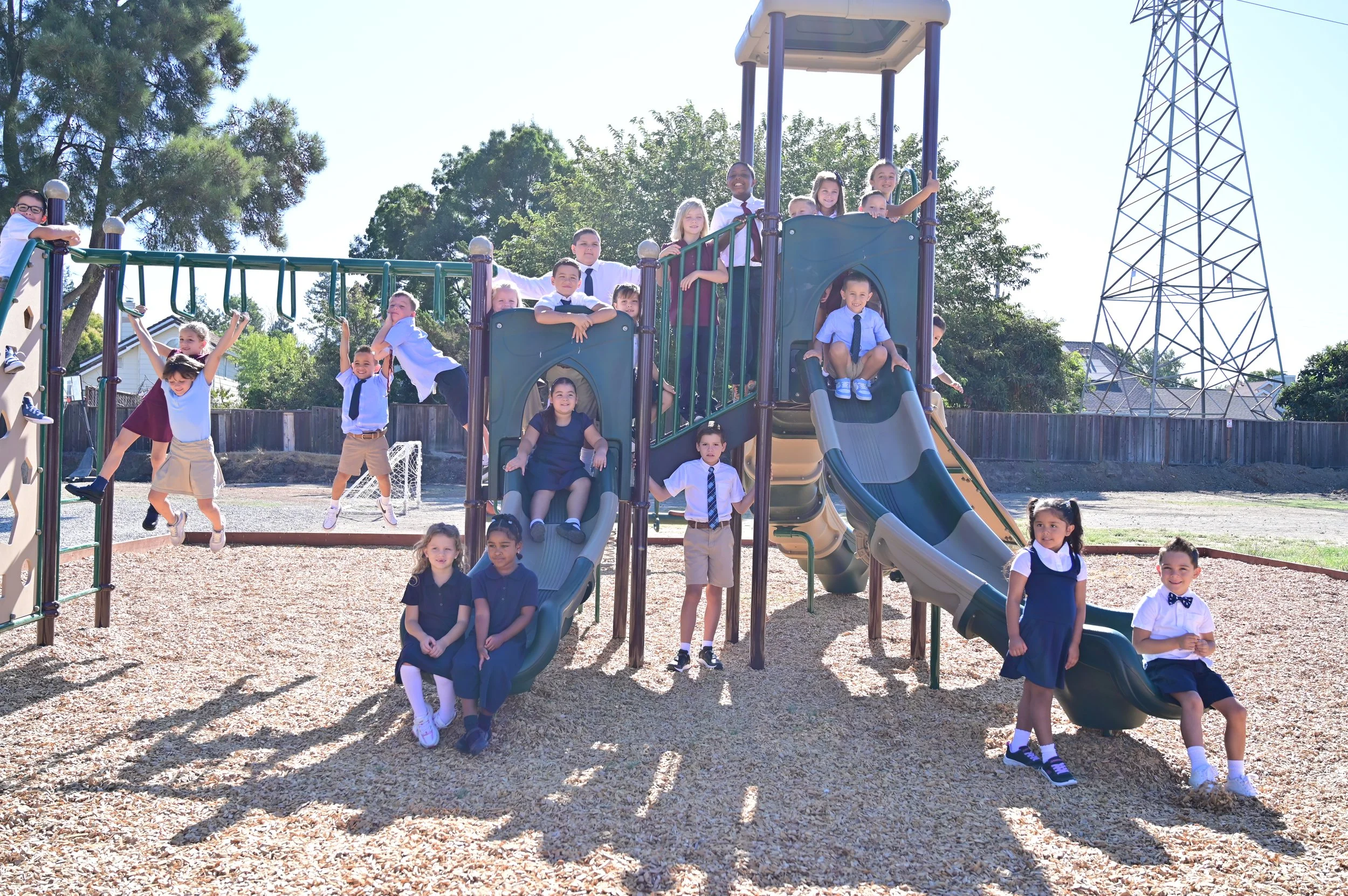 Group of children wearing school uniforms playing on a playground with slides and climbing structures outdoors