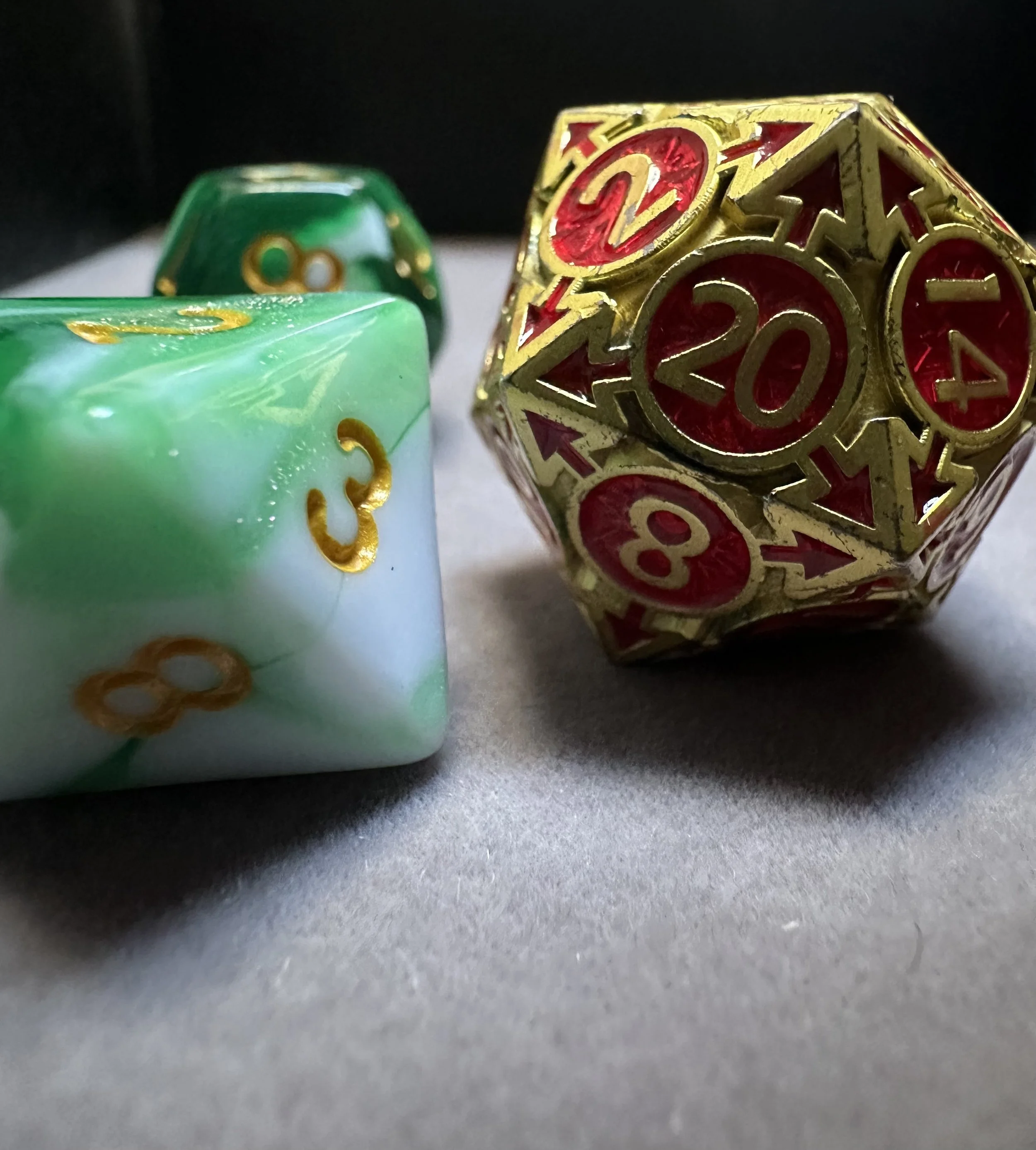 Close-up of three colorful polyhedral dice used for tabletop role-playing games, with a focus on a red and gold twenty-sided die showing 20, surrounded by a green and white die showing 3, and a small green die in the background.