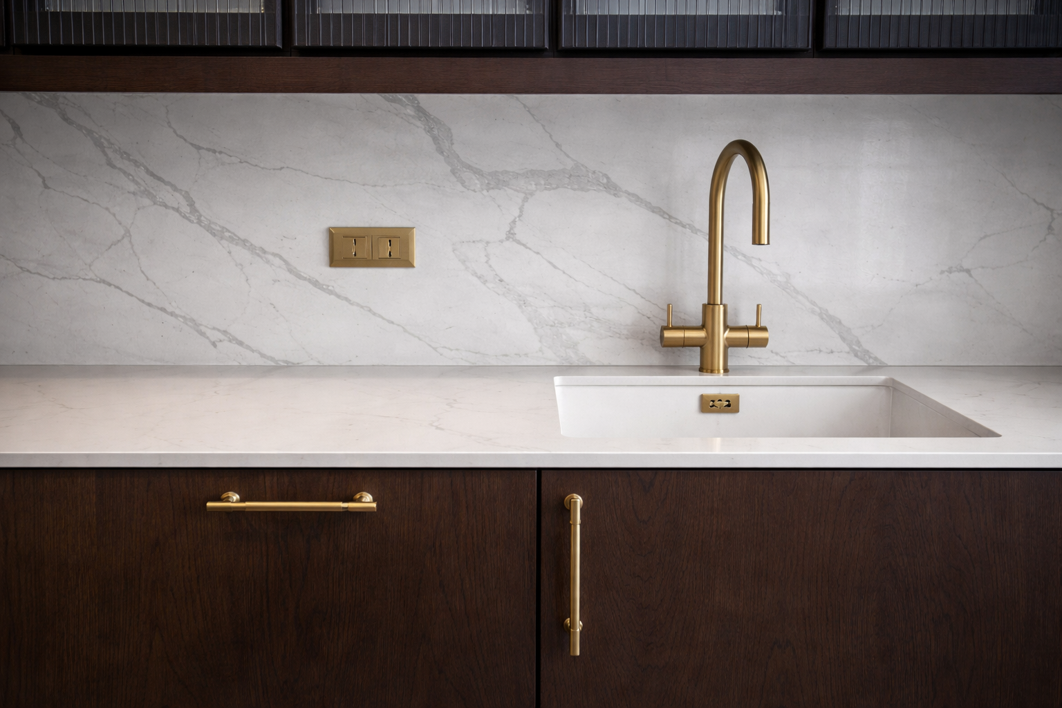 Modern kitchen sink with gold faucet, marble backsplash, and dark wooden cabinets.