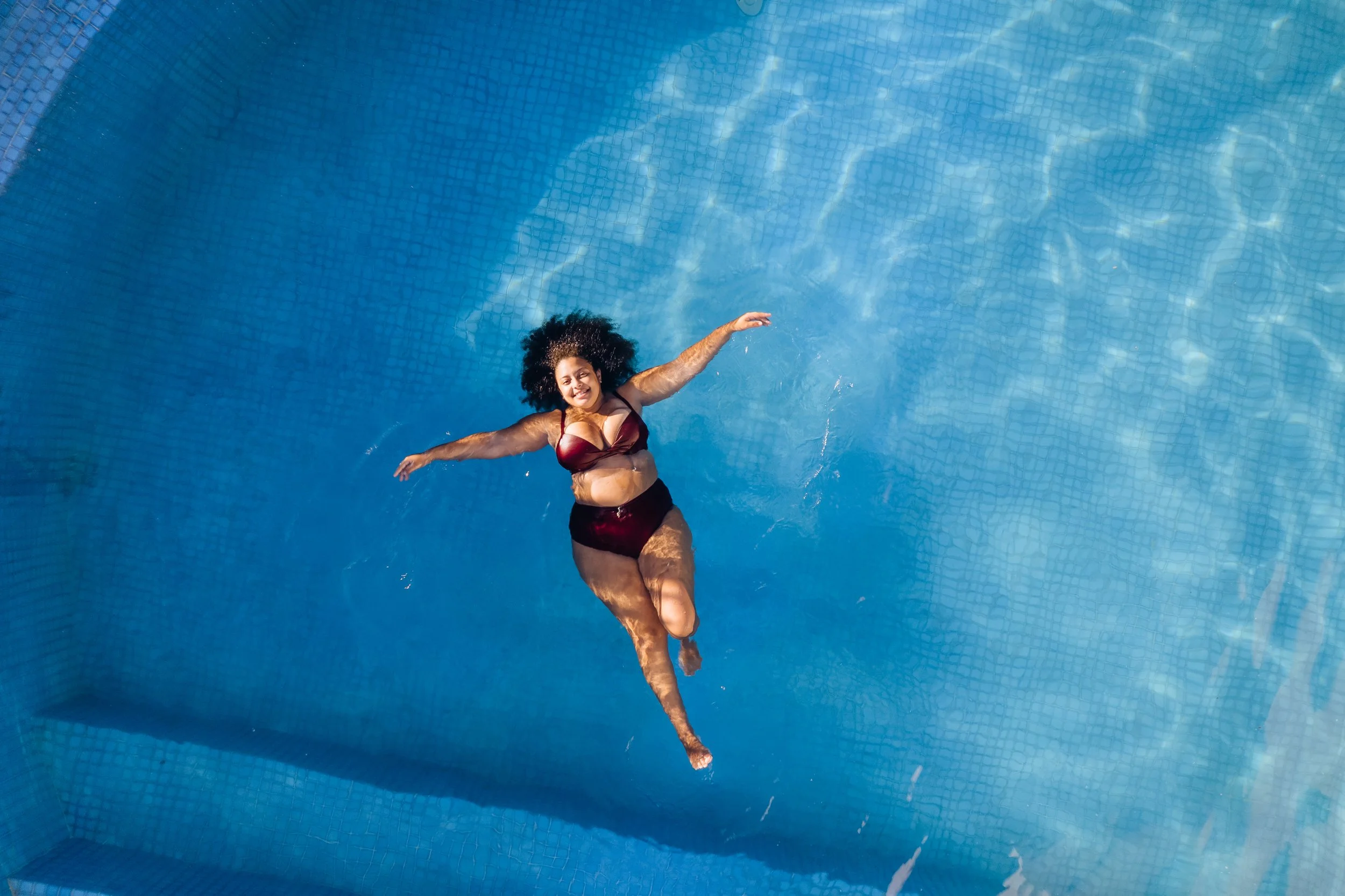 Woman in a two-piece swimsuit floating on her back in a swimming pool with light reflecting on the water.