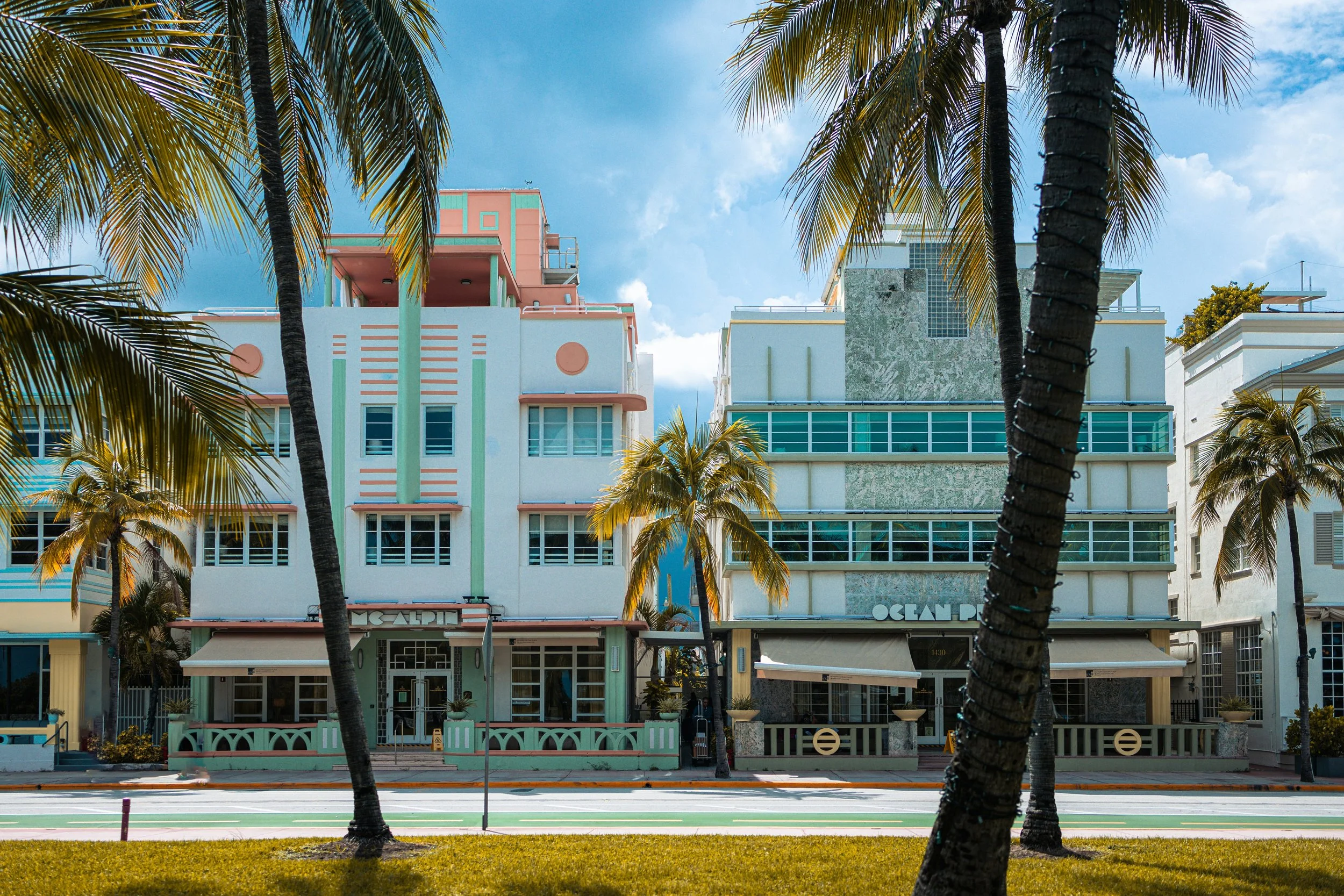 Colorful Art Deco buildings with palm trees in front under a partly cloudy sky.