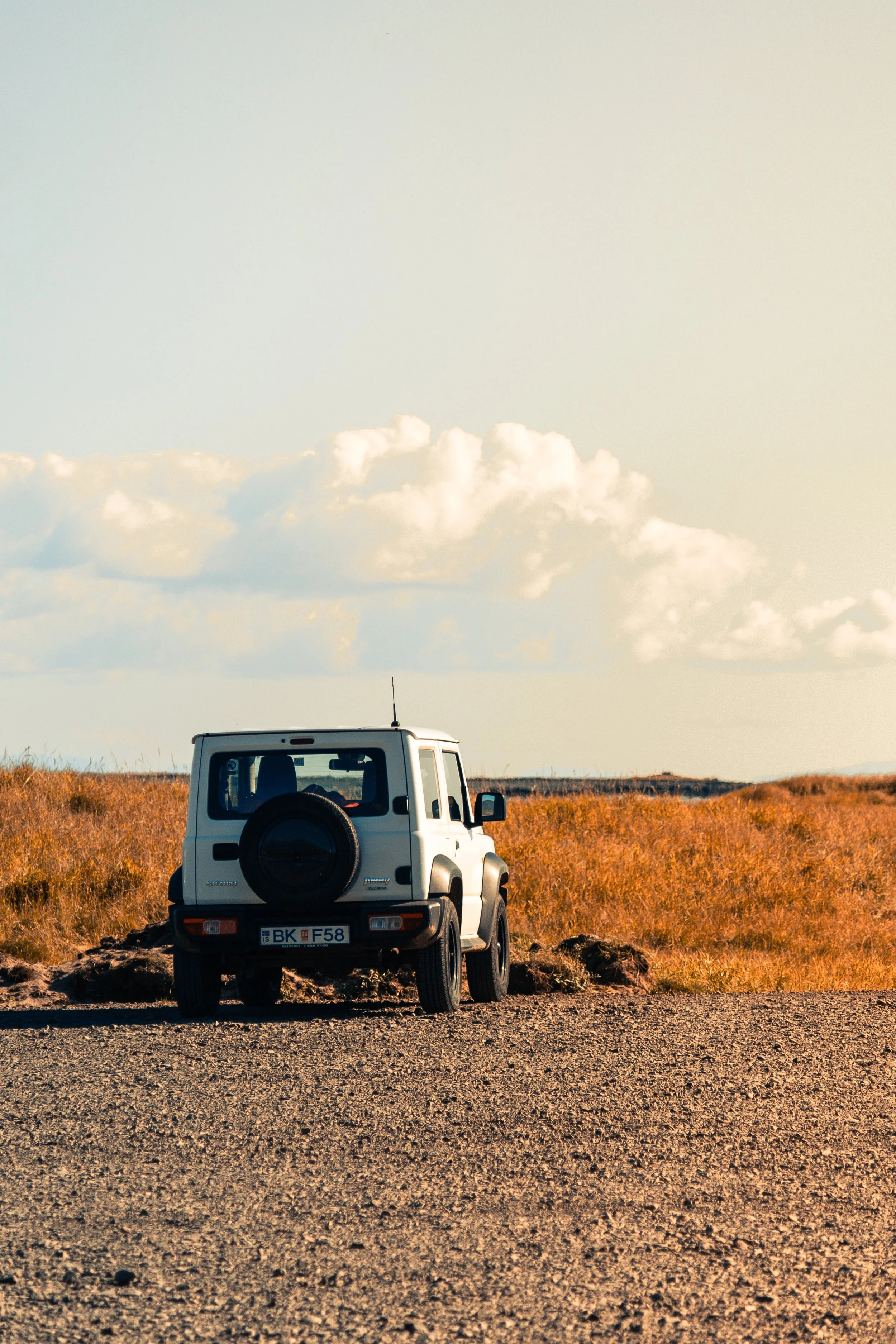 A white off-road vehicle parked on a dirt road in a barren landscape with dry grass, under a partly cloudy sky.