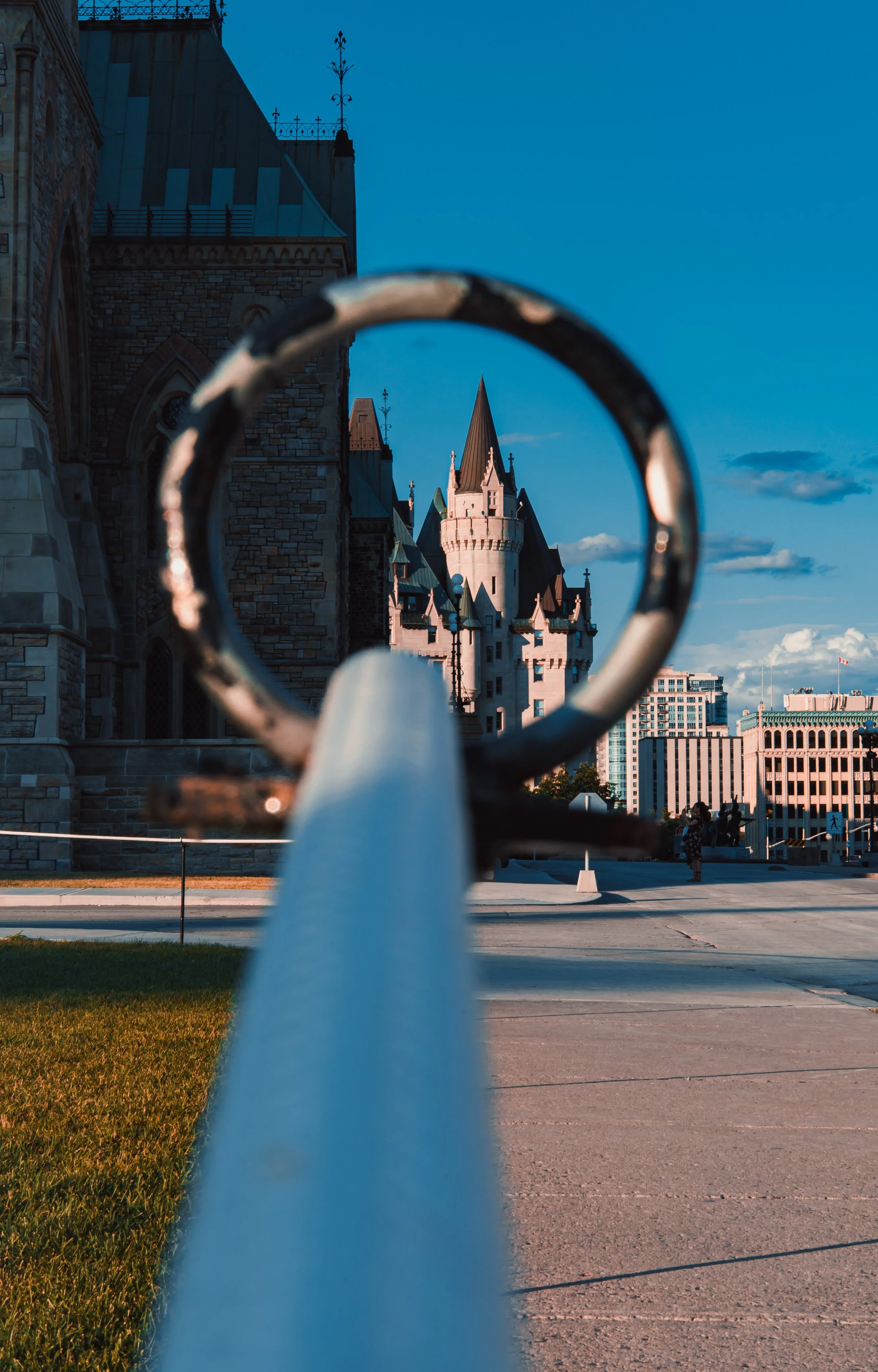 A castle with pointed towers is viewed through a metal railing in an urban setting on a clear day with blue skies.