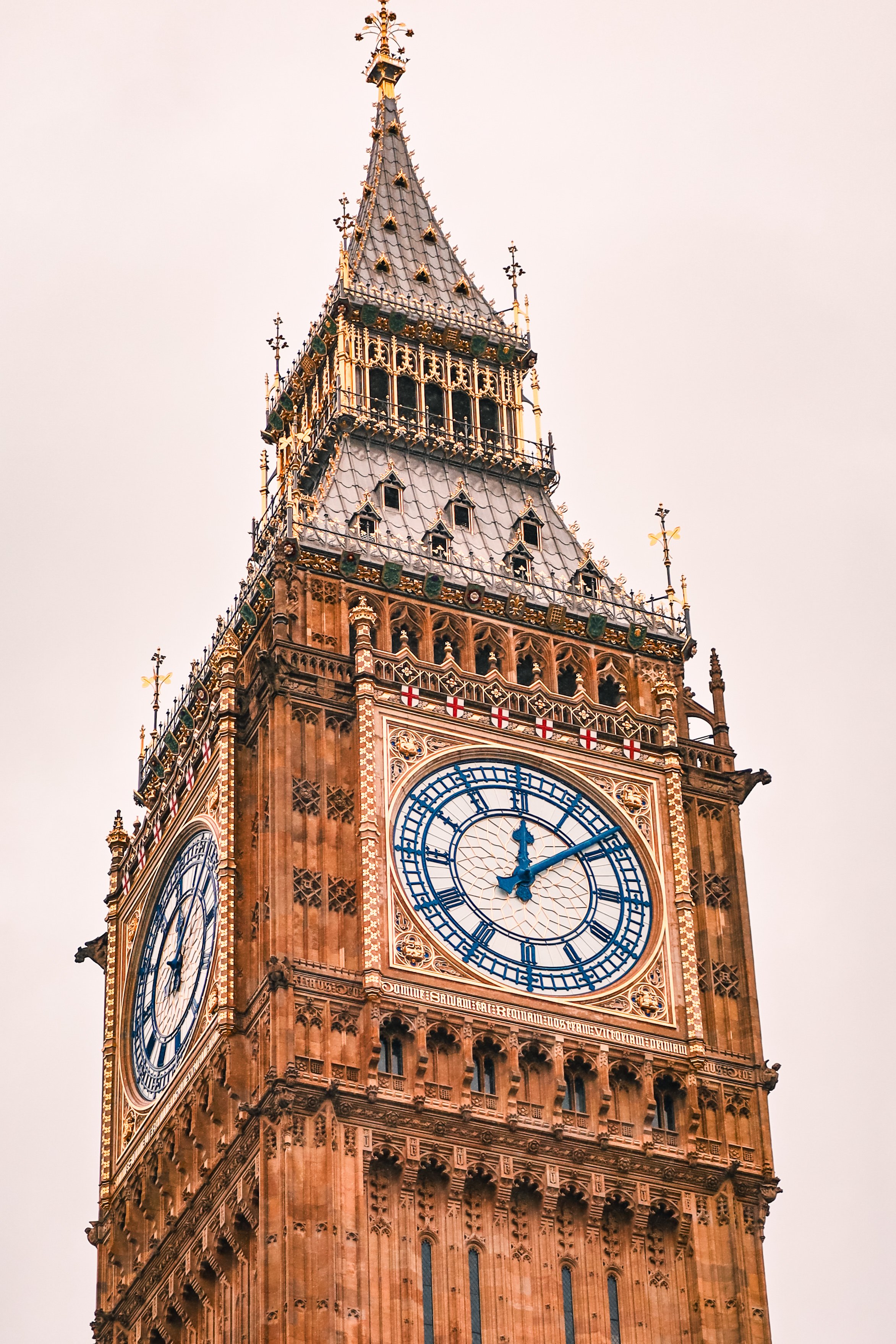 Close-up of Big Ben clock tower in London, showing the time at 12:10, with intricate Gothic architecture details and a cloudy sky in the background.