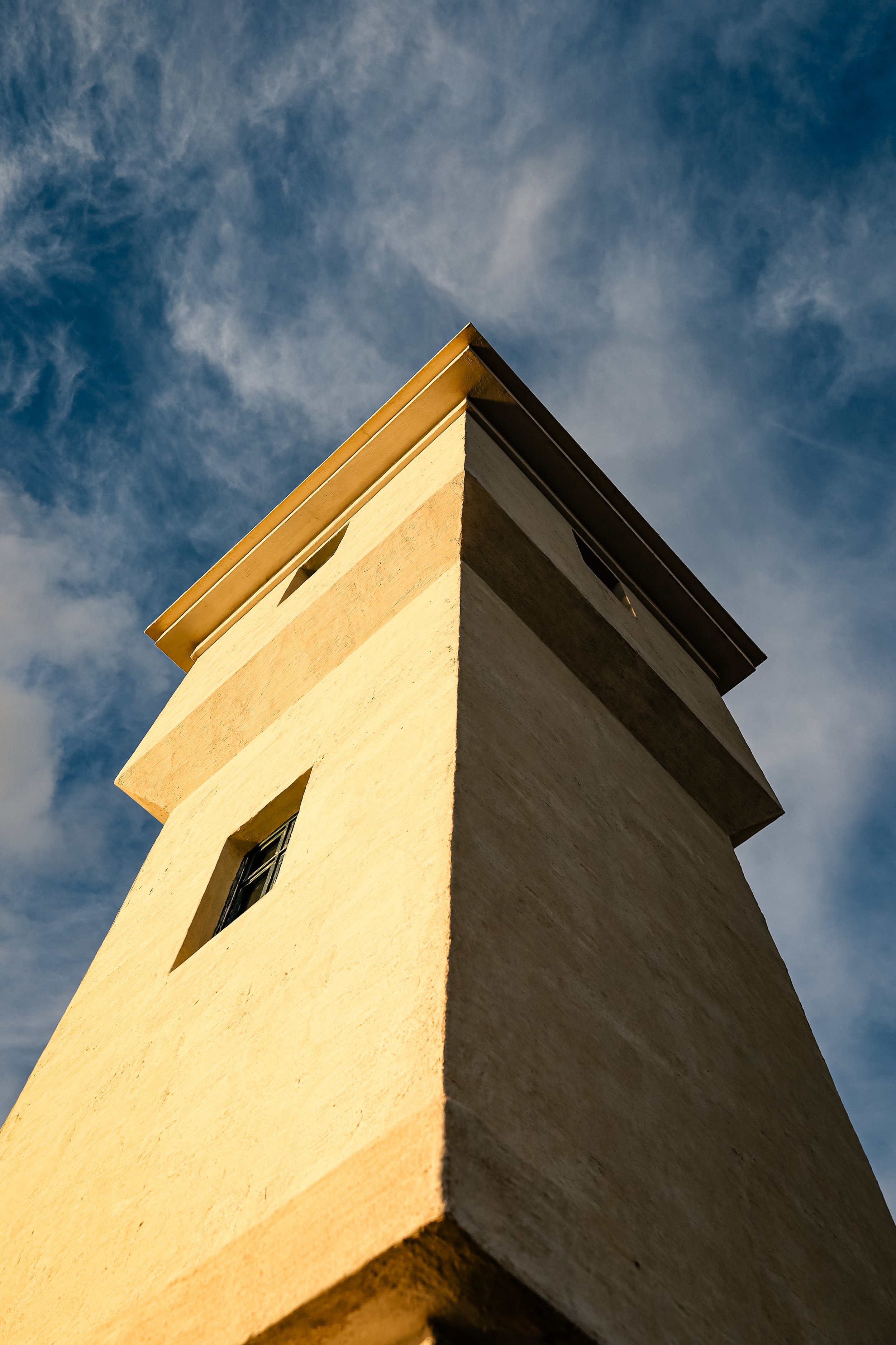 A yellow apartment building seen from below against a blue sky with wispy clouds.