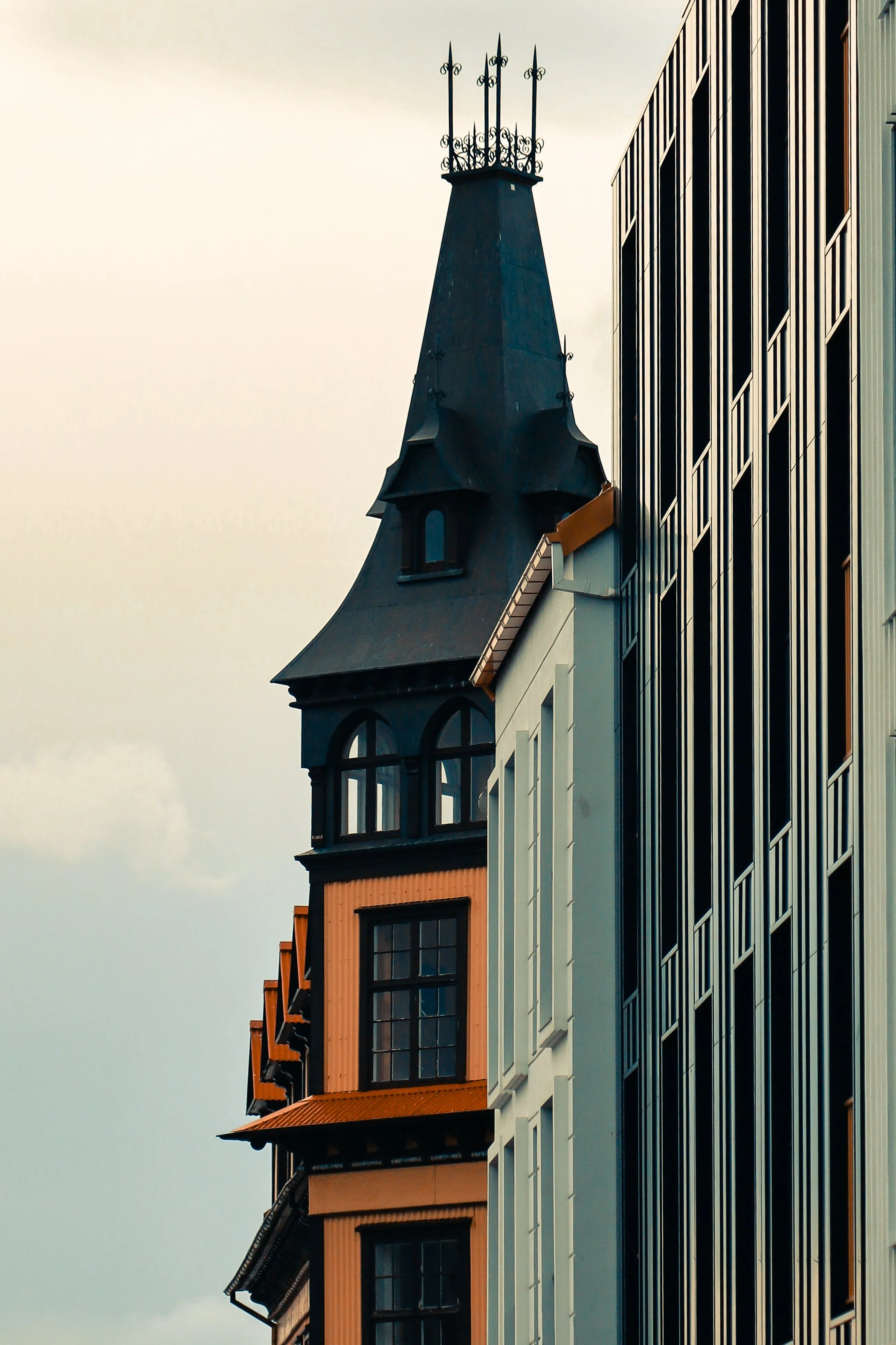 Close-up of historic and modern buildings, focusing on their rooftops and facades, with a cloudy sky in the background.