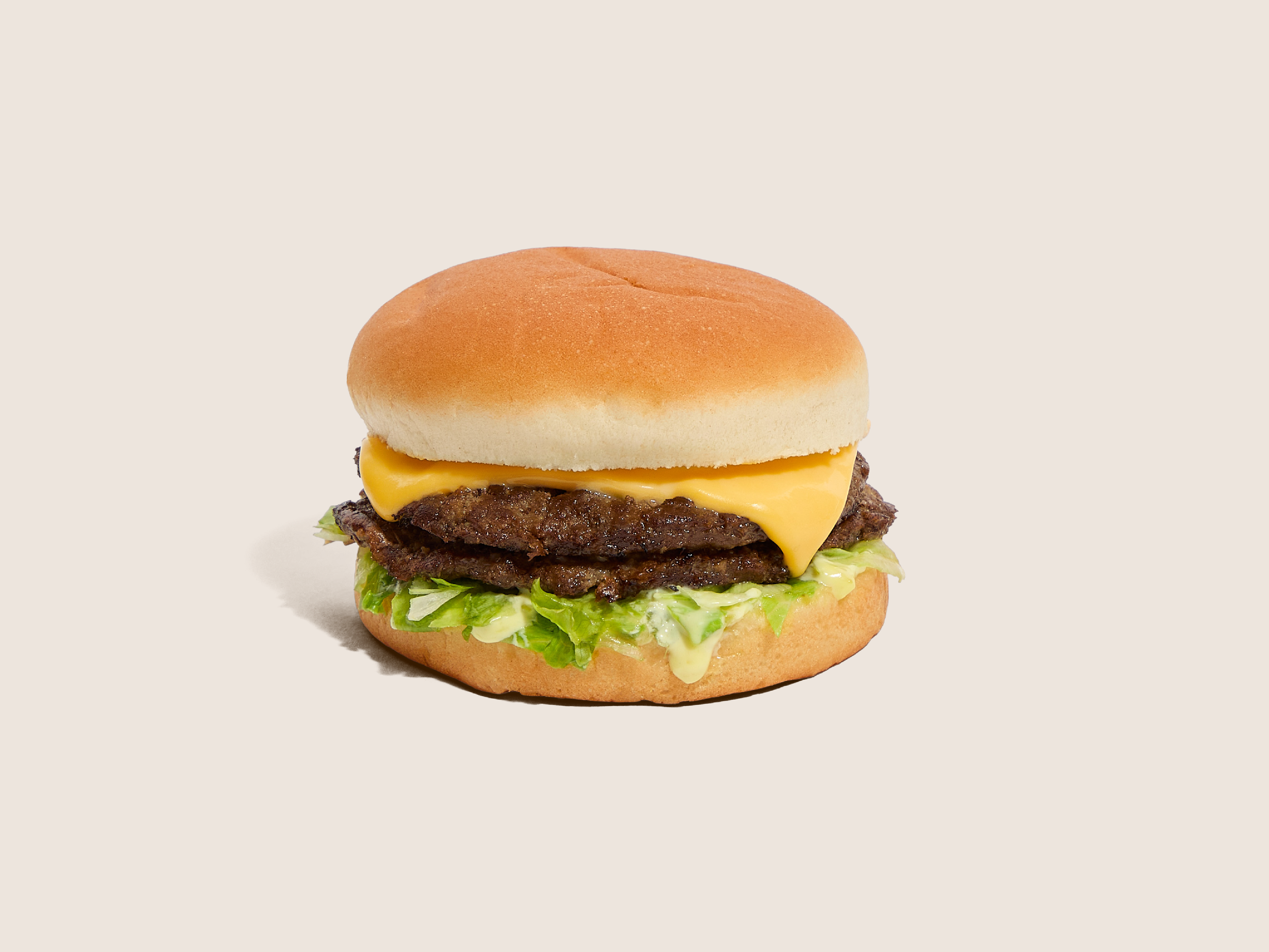 A Dick's Drive-In Deluxe burger with two beef patties, melted cheese, lettuce, sweet-relish sauce, and a bun, on an off-white background.