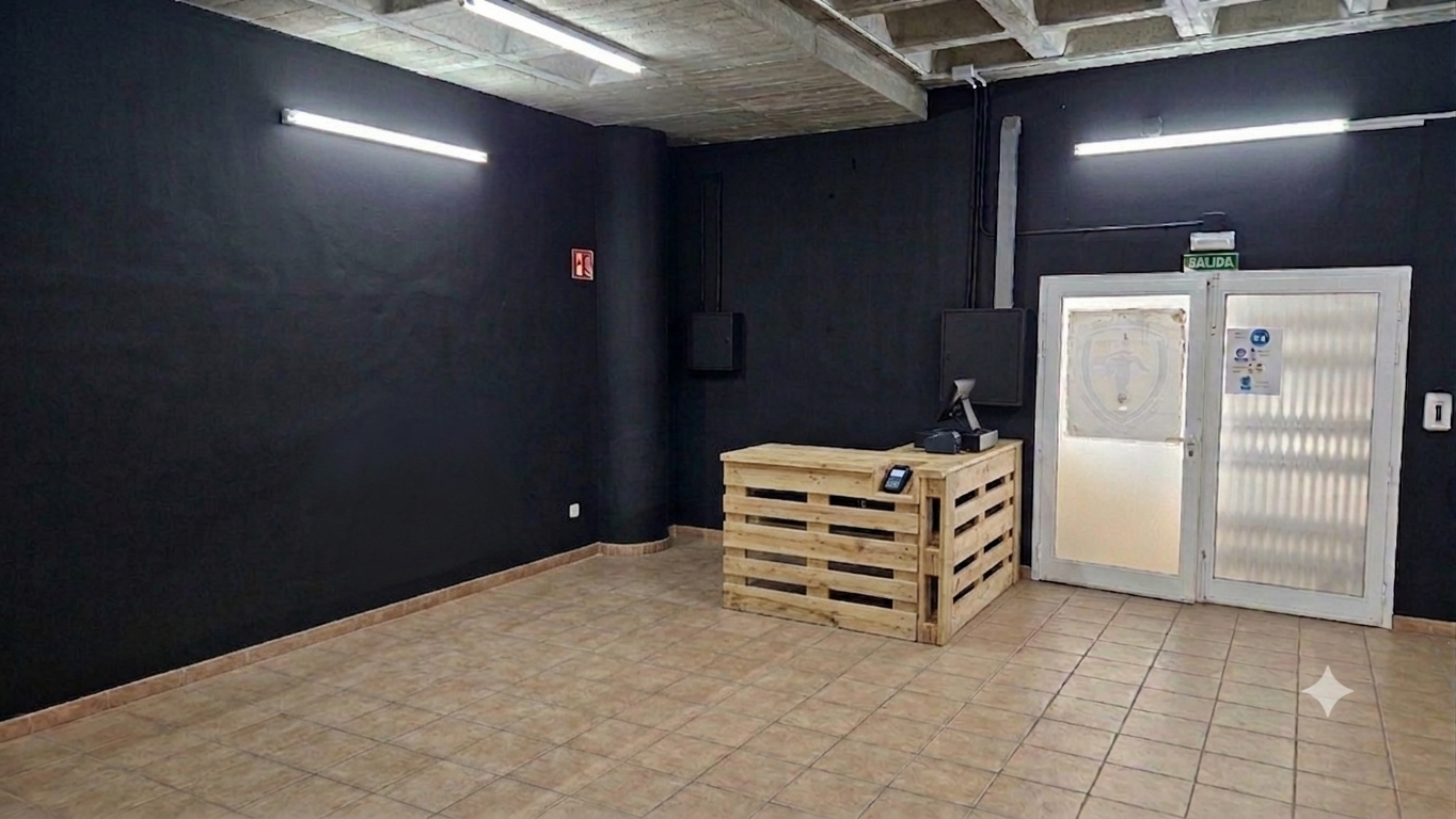 Vestíbulo con paredes negras, suelo de baldosas, iluminación fluorescente, puerta de salida con cartel de 'salida' y vestíbulo con mostrador de madera con caja registradora y teléfono.