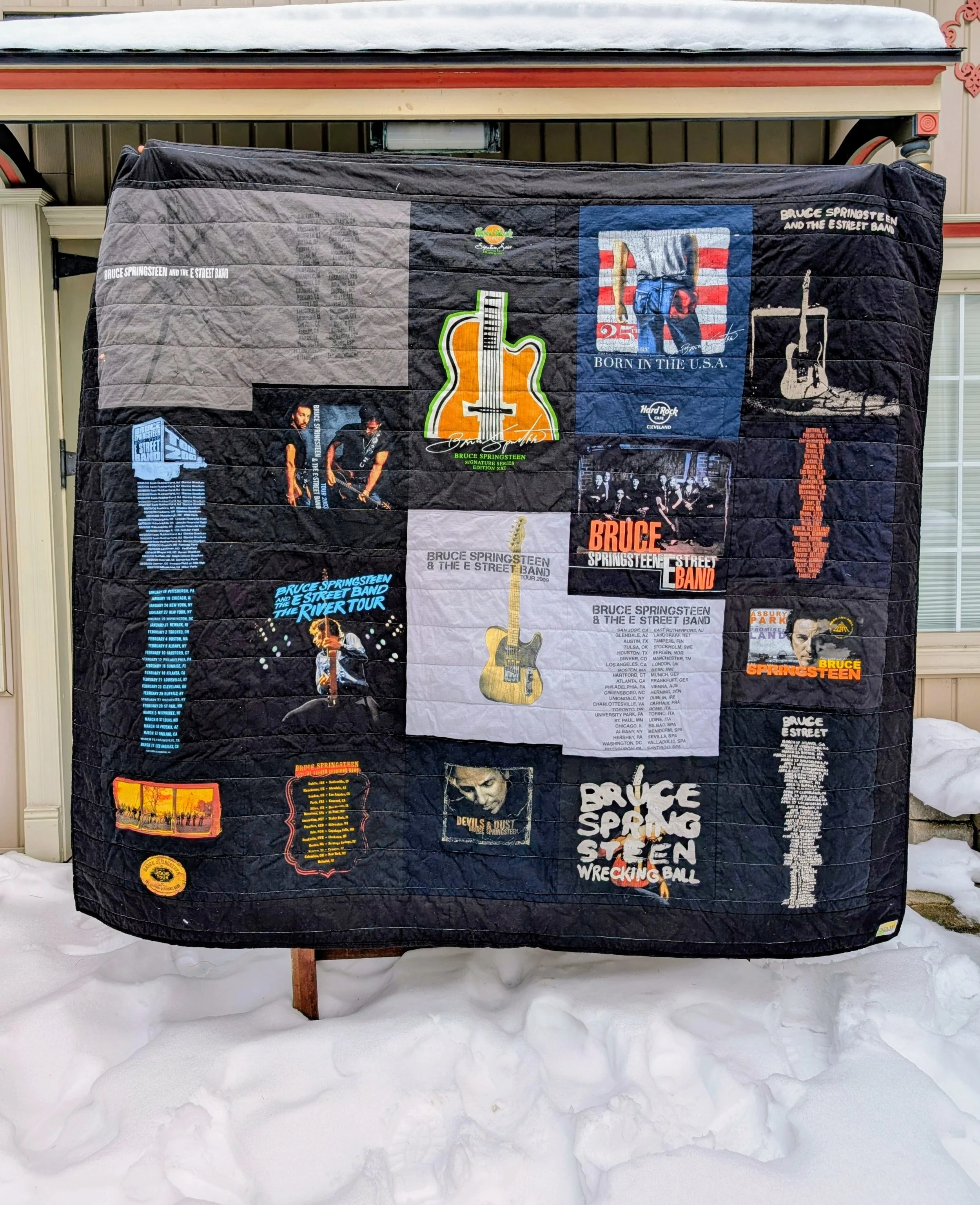 A quilt featuring Bruce Springsteen memorabilia, including various concert posters, album covers, and images of the musician with snow on the ground in the background.
