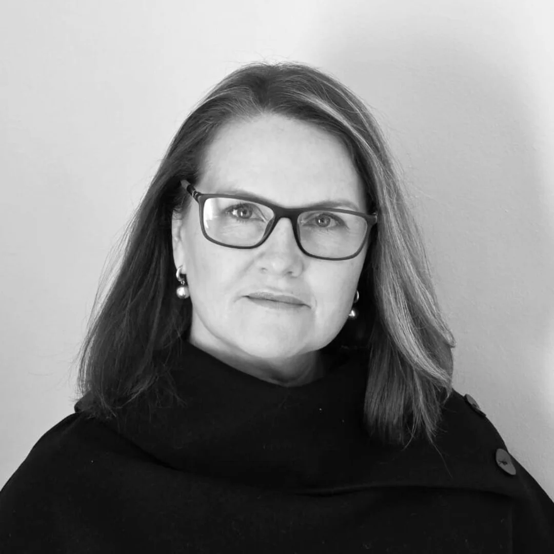 Black and white portrait of a woman with shoulder-length hair wearing glasses and earrings, looking directly at the camera.