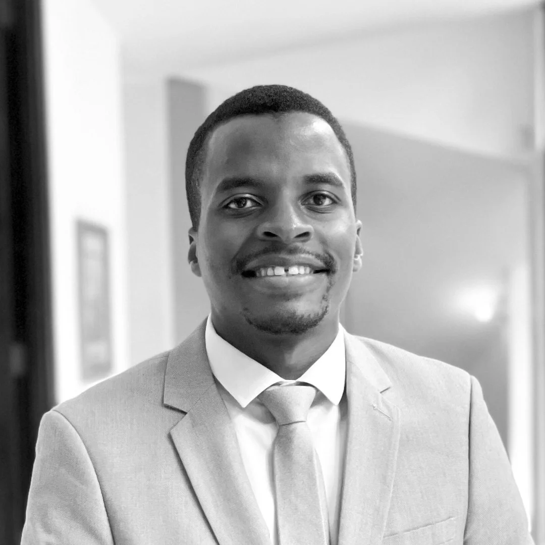 A smiling man in a suit and tie, with short hair, in a professional setting.