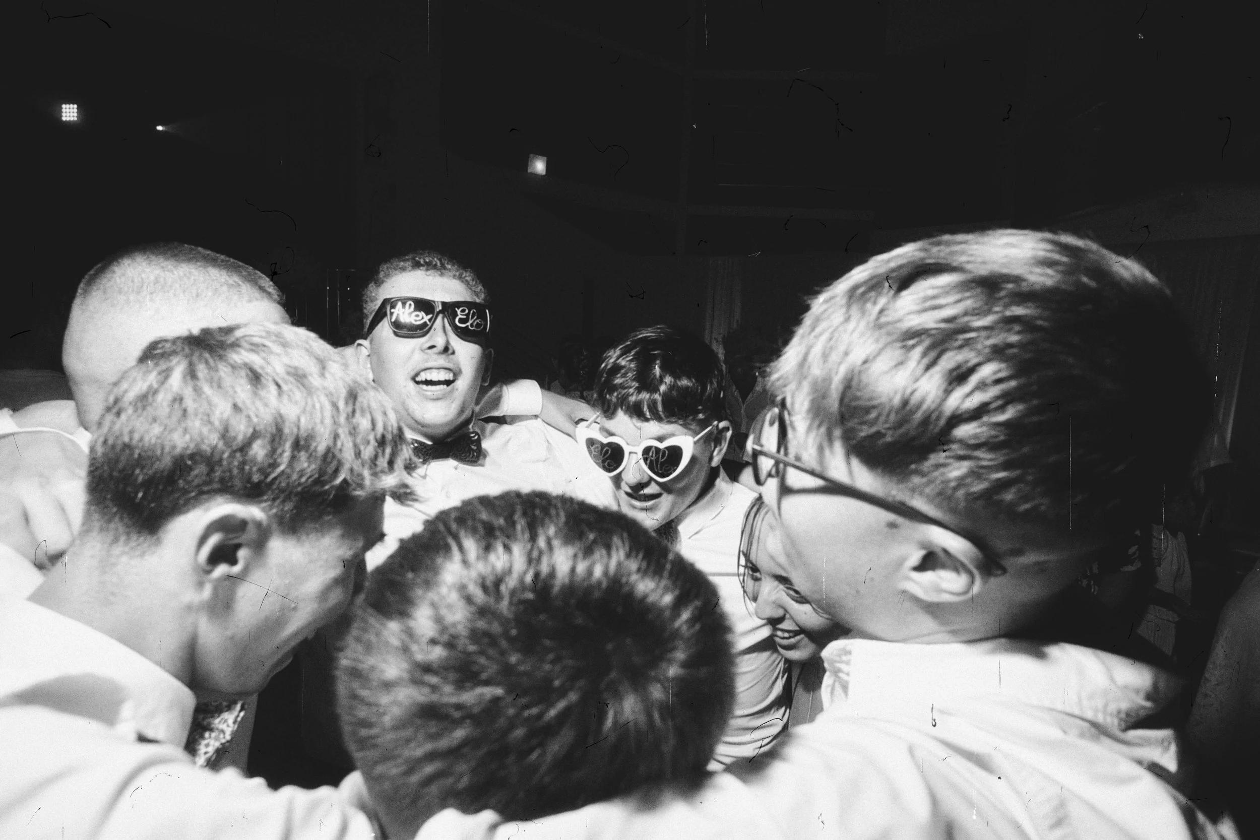 Groupe de jeunes hommes souriant, portant des lunettes de soleil, lors d'une fête ou d'une célébration.