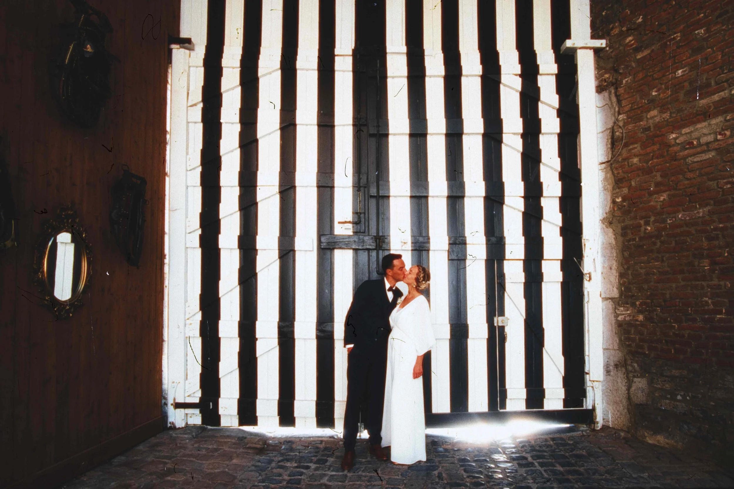 Un couple en mariée et en costume s'embrassent dans une porte en bois avec des rayures blanches et noires.