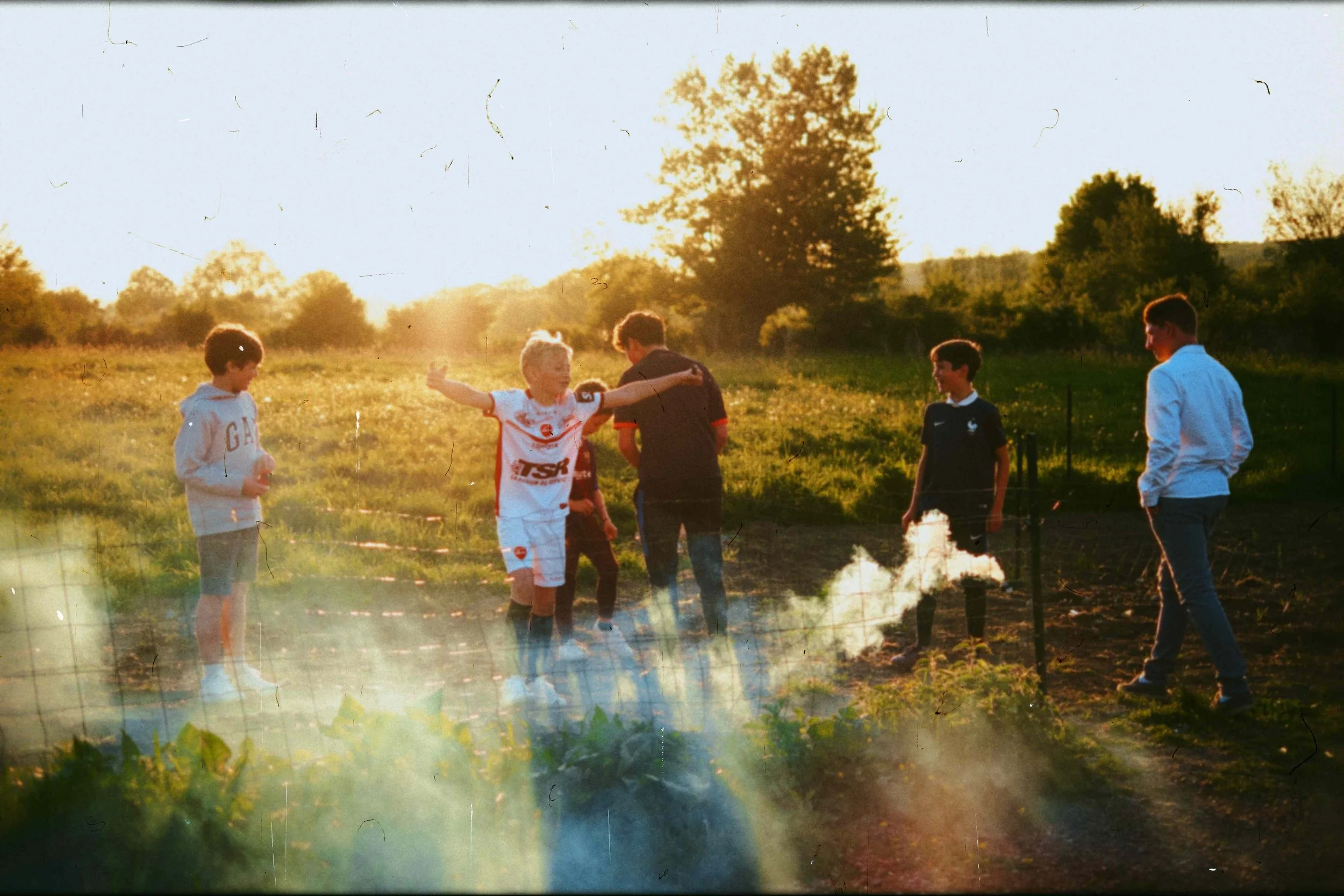 Groupe de jeunes garçons jouant dans un champ en plein air lors d'un coucher de soleil, certains souriants et en mouvement, portée décontractée et sport.
