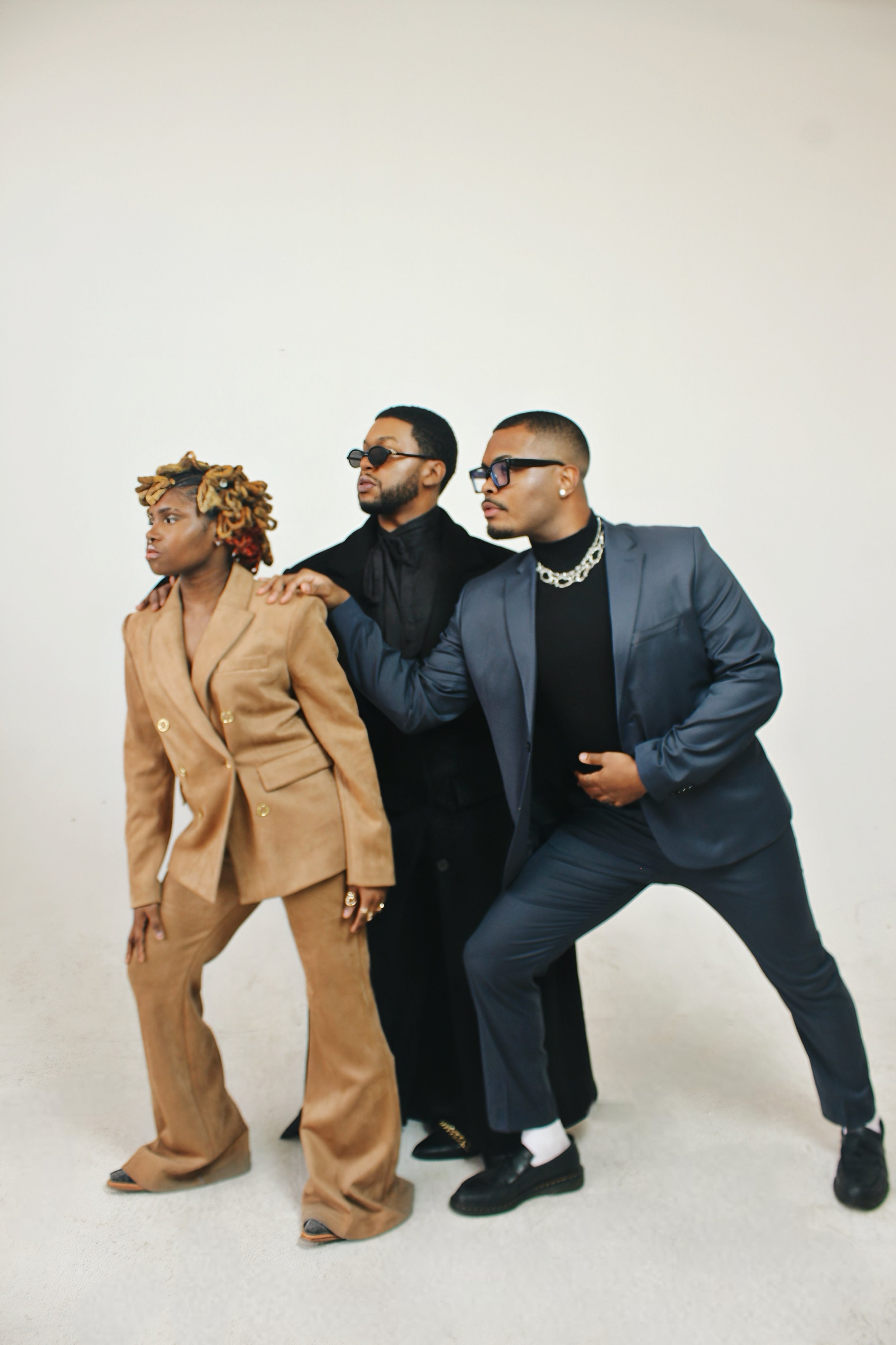 Three stylish individuals posing together against a plain white background, dressed in fashionable clothing and accessories.