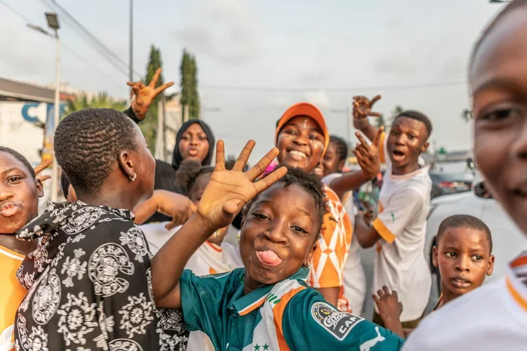 Group of children smiling and waving in an outdoor setting.