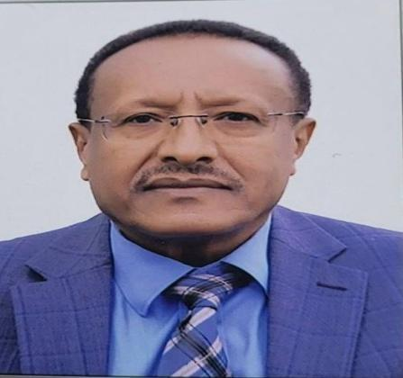 A man in a blue suit and tie with glasses, serious expression, plain white background.
