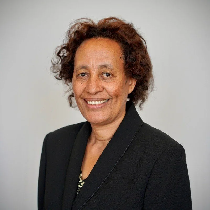 A woman with short curly hair wearing a black blazer and smiling.
