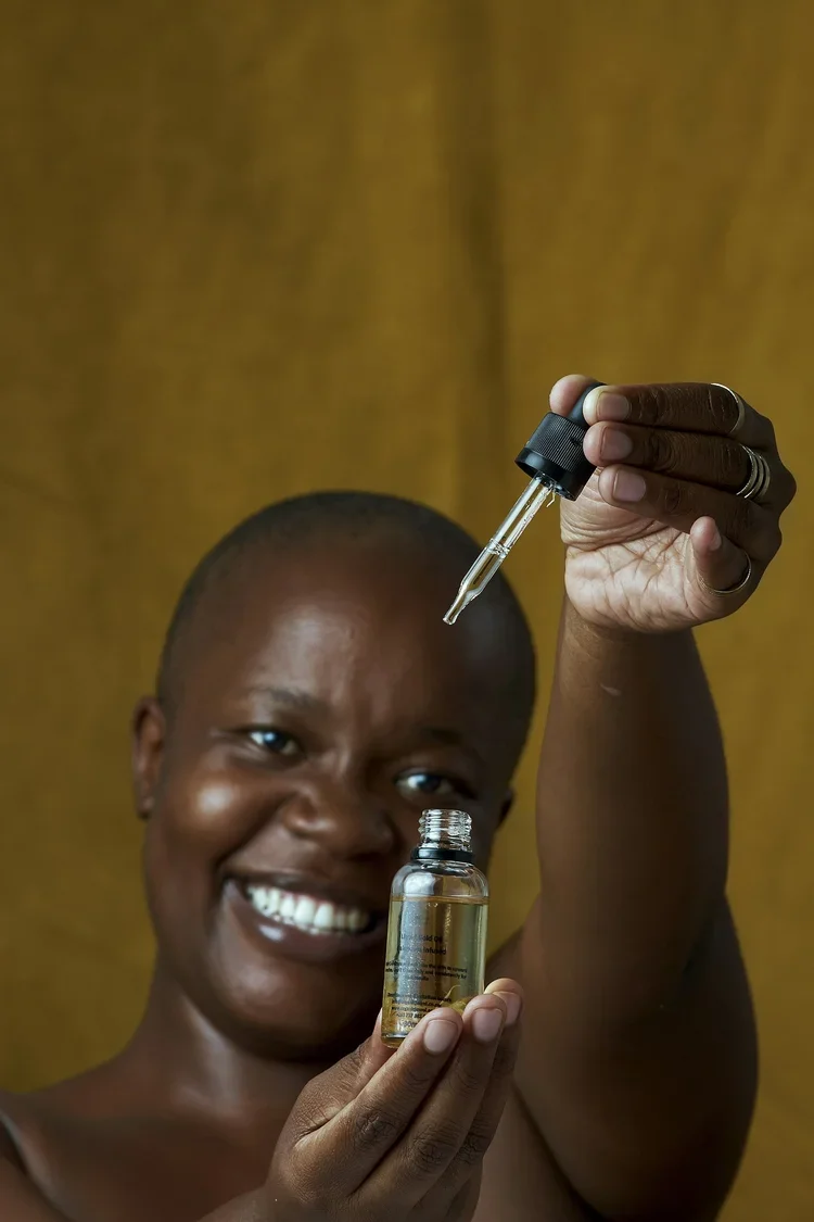 Person holding a small bottle of skincare serum and a dropper, smiling and looking at the camera.