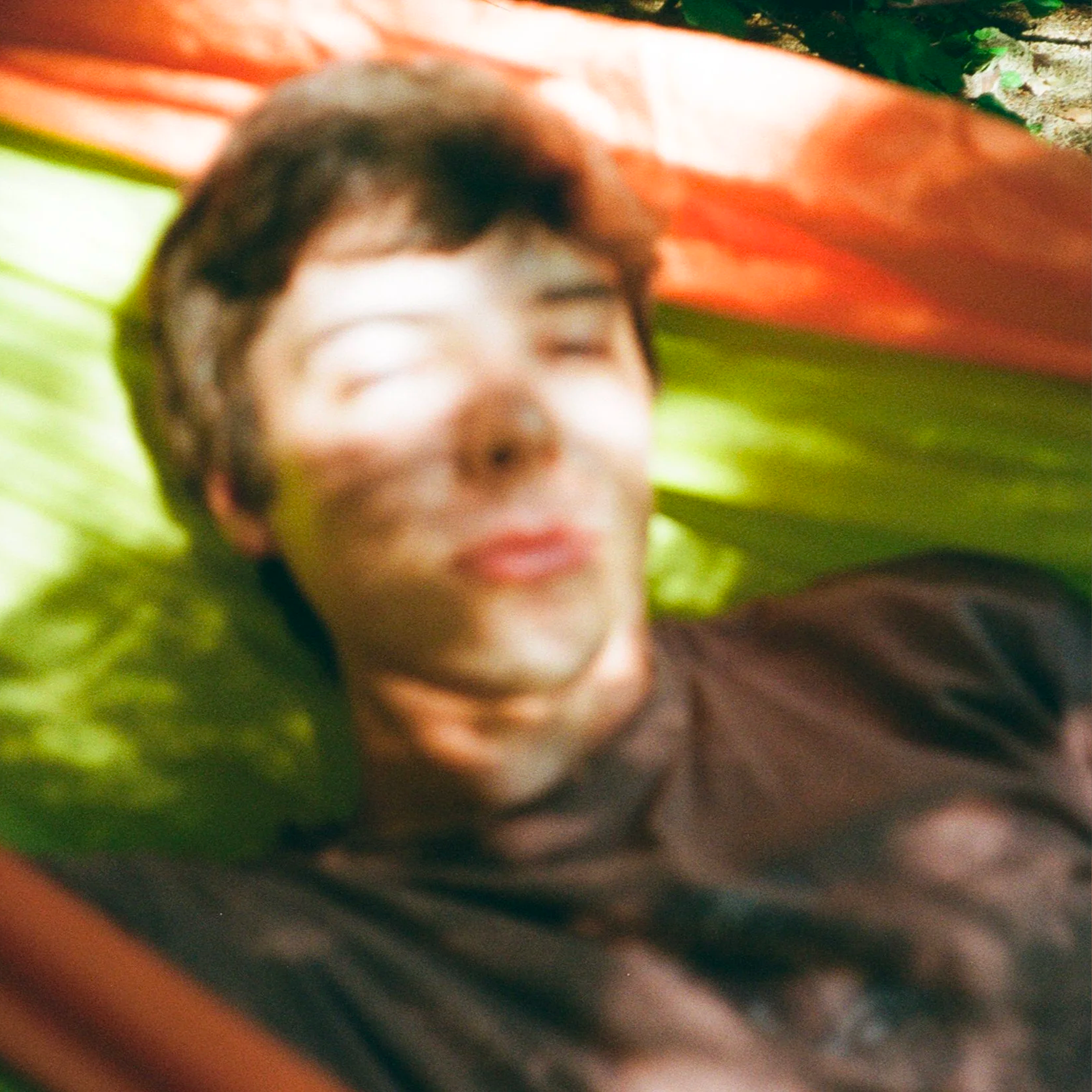A person with short dark hair lying on a colorful hammock with their eyes closed and lips puckered.