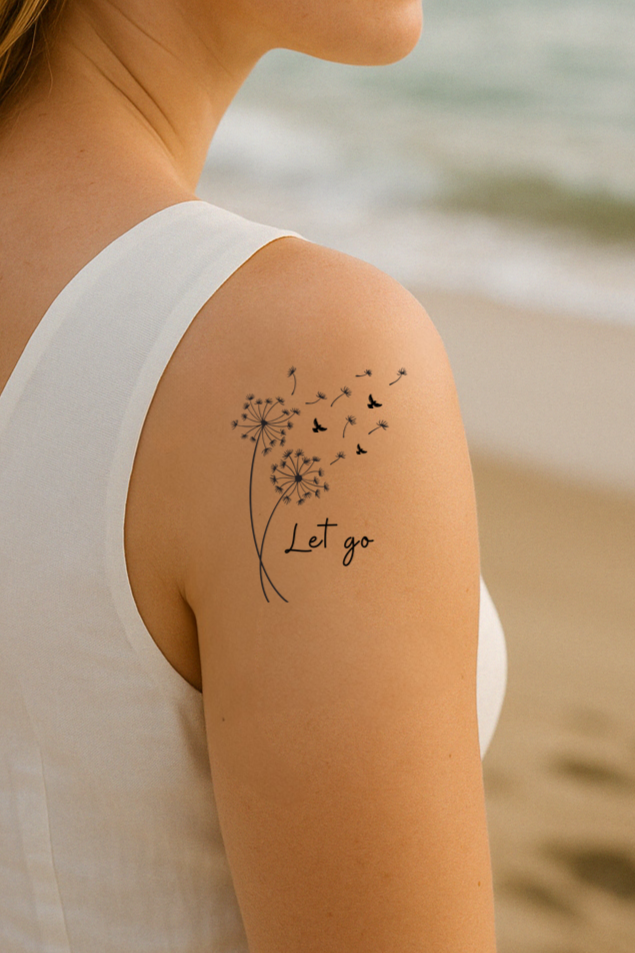 Blond female with light skin color is at the beach. Her eyes are closed and she has a tattoo on her shoulder that says "let go". This tattoo has dandelions flying away. 