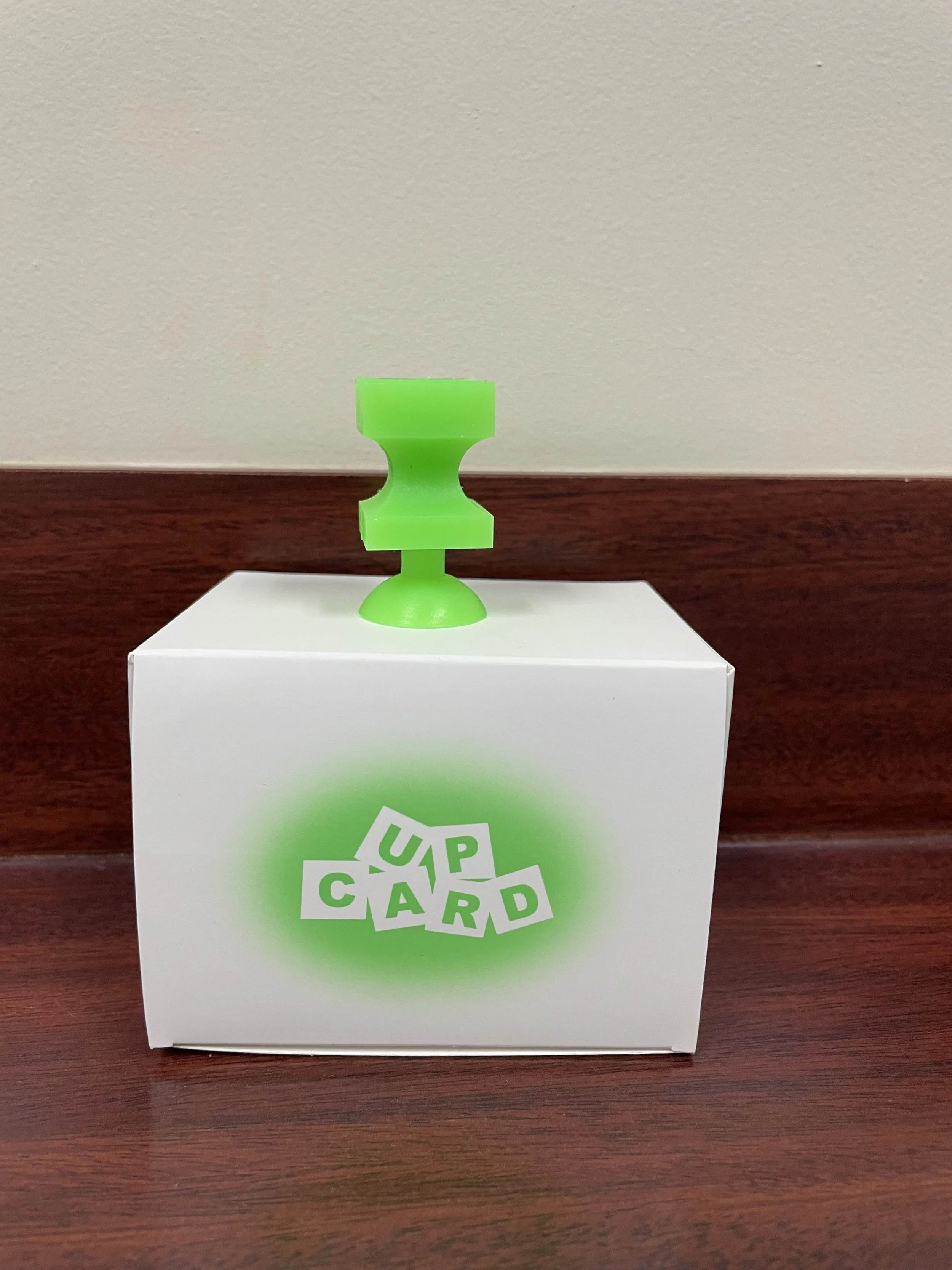 The product, which is a bright green silicone card picker upper on top of the paper box that it comes in.