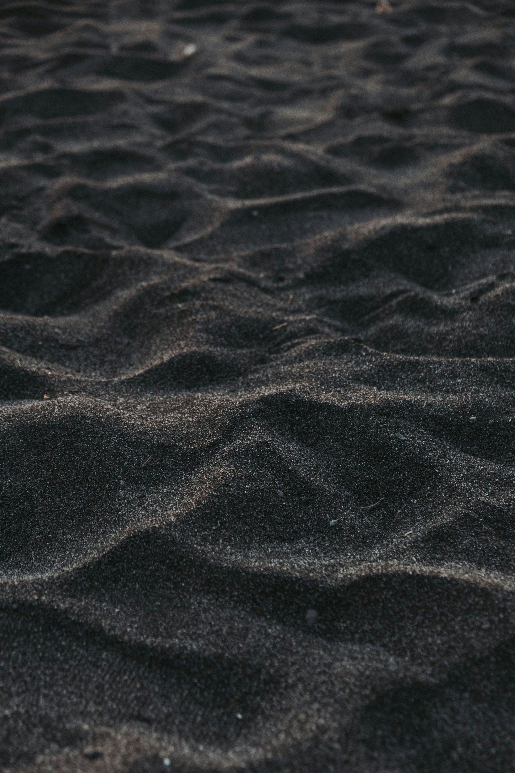 Close-up of dark sandy beach with textured ripples in the sand.