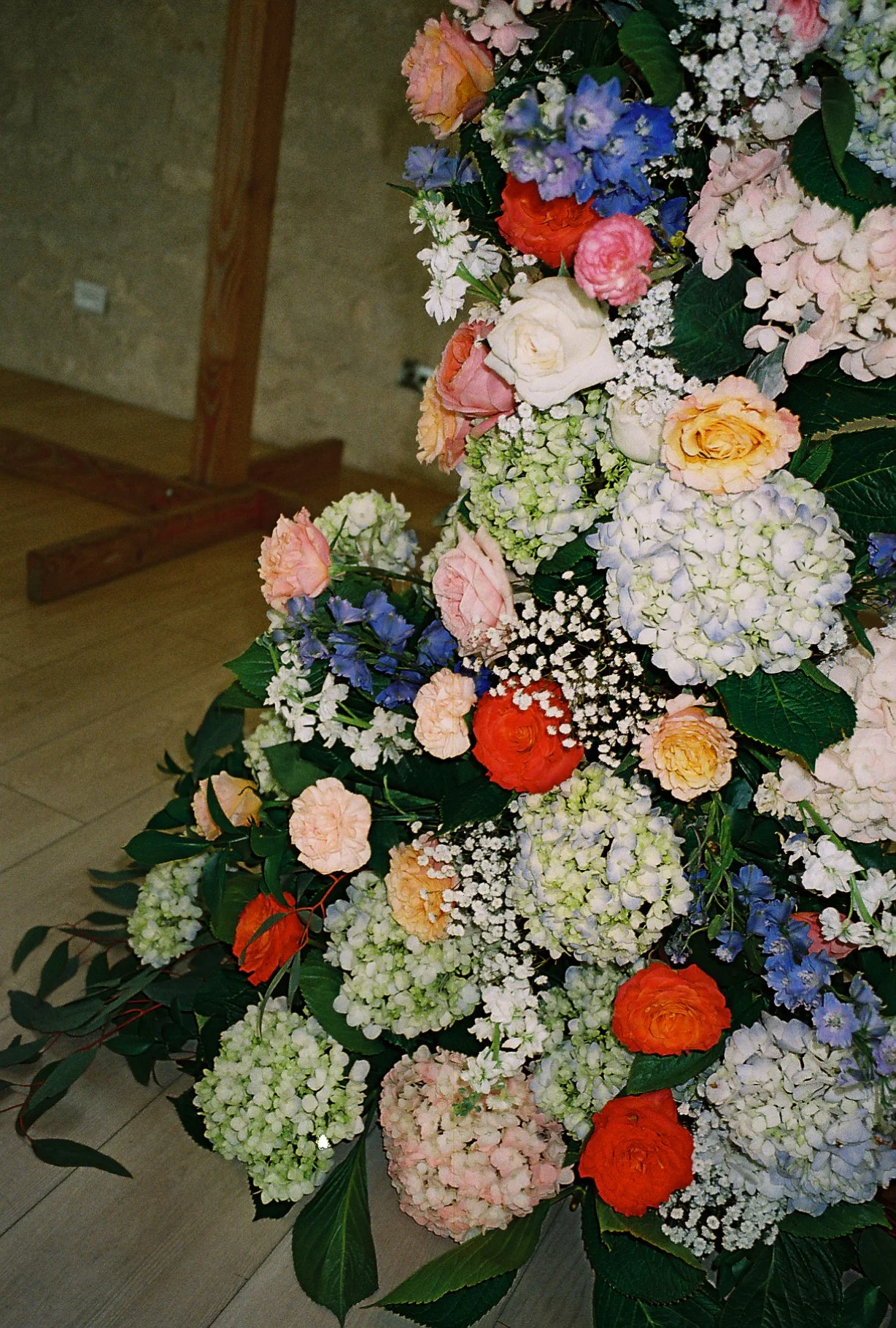 A colorful floral arrangement featuring white, pink, orange, and blue flowers, with green leaves and some baby's breath.