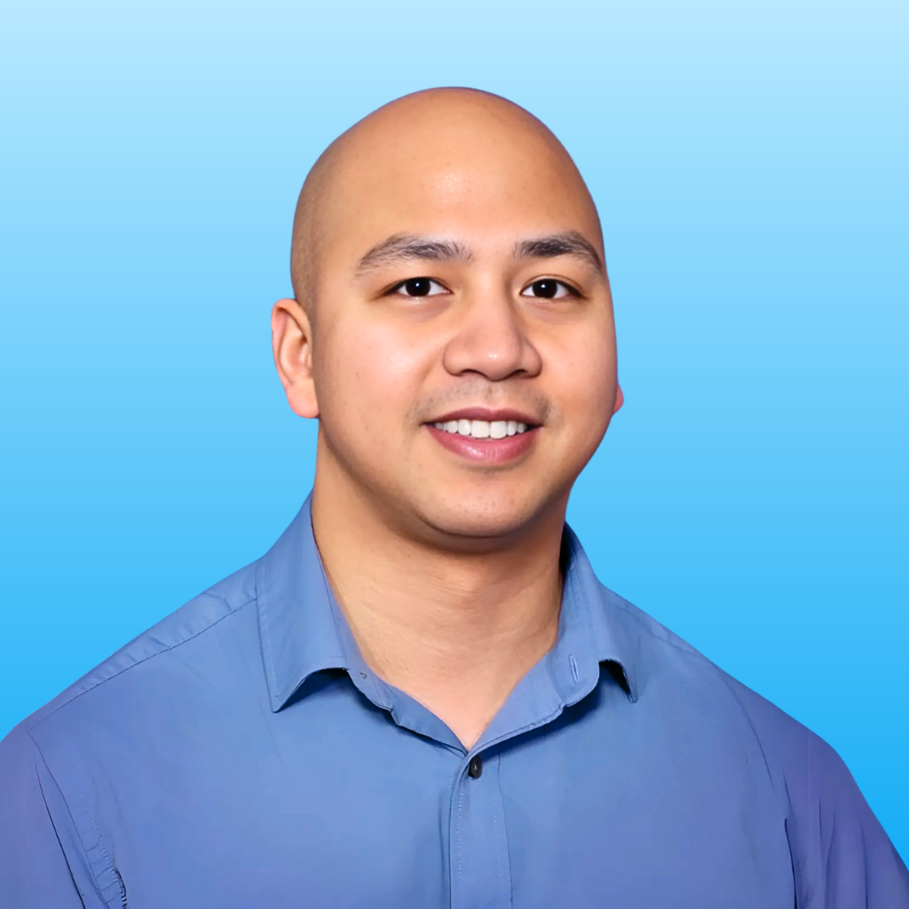 A close-up portrait of a male physical therapist wearing a blue button-up shirt, smiling against a blue gradient background.