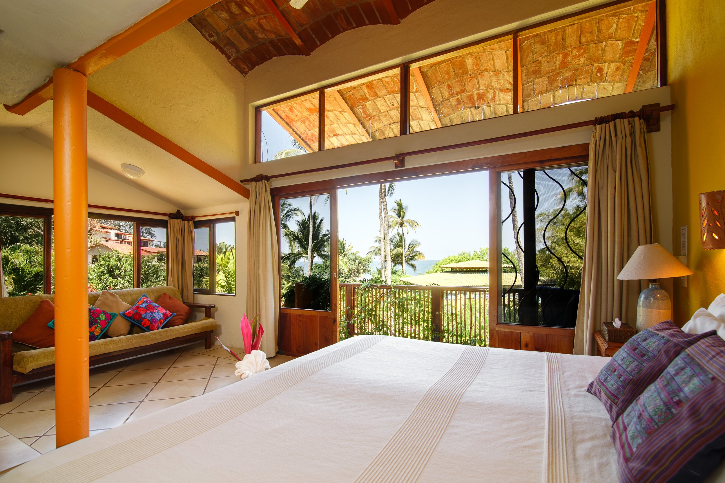 a guest suite at Mar de Jade with tile floors, wood details, arched ceiling and colorful embroidered pillows Mexican textiles and colo