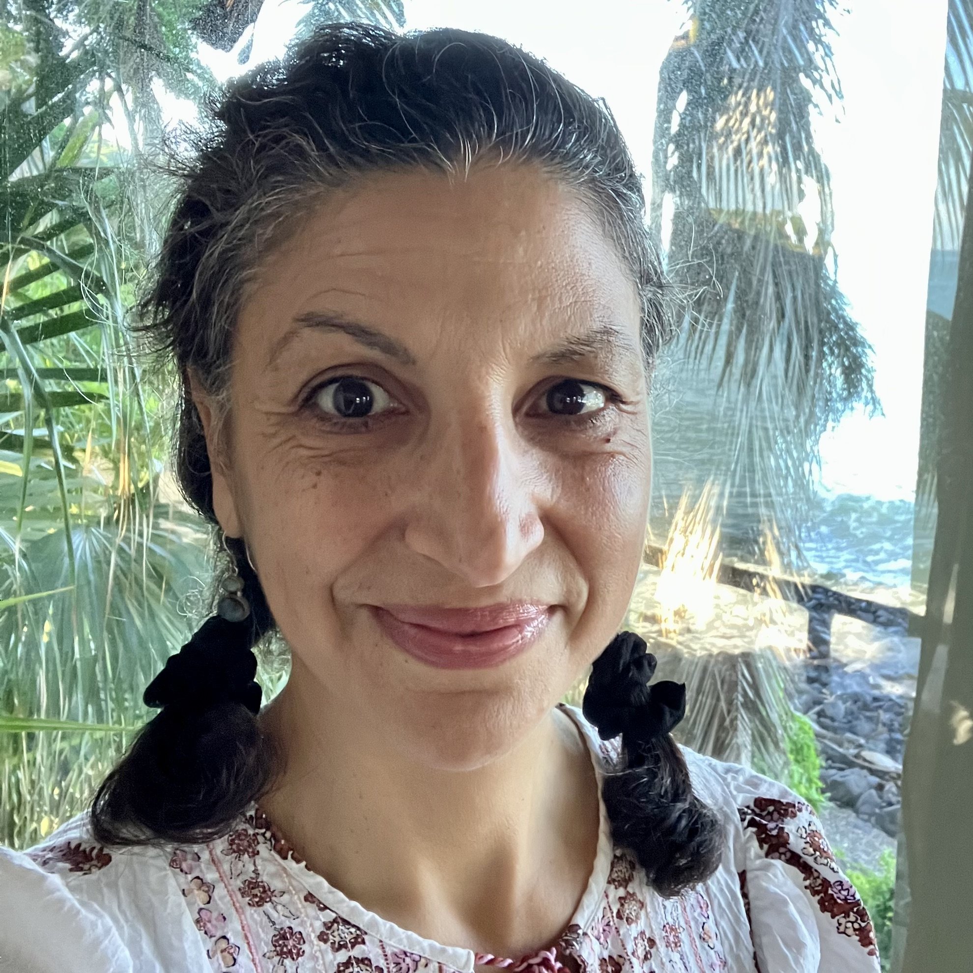 Elise Constantine, Licensed Massage Therapist and specialist in acupressure and traditional Thai Massage. Certified Yoga and Qi Gong Teacher pictured at Mar de Jade Retreat Center with palm fronds and ocean vistas outside the studio