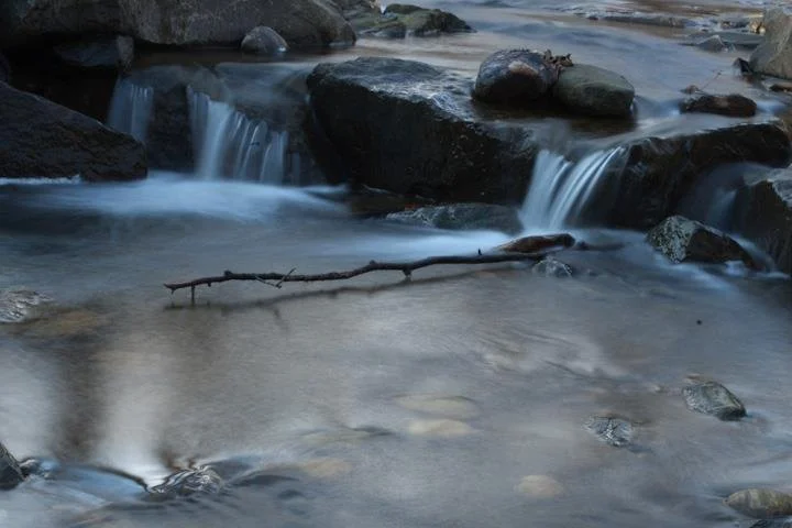 A timed exposure color photograph of a creek with a small waterfall